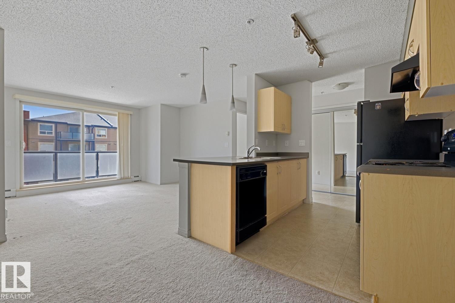 Open-concept living area featuring a kitchen island, track lighting, and a full-height sliding glass door - #312 13908 136 St Nw, Edmonton, AB - Indoor Photo Showing Kitchen
