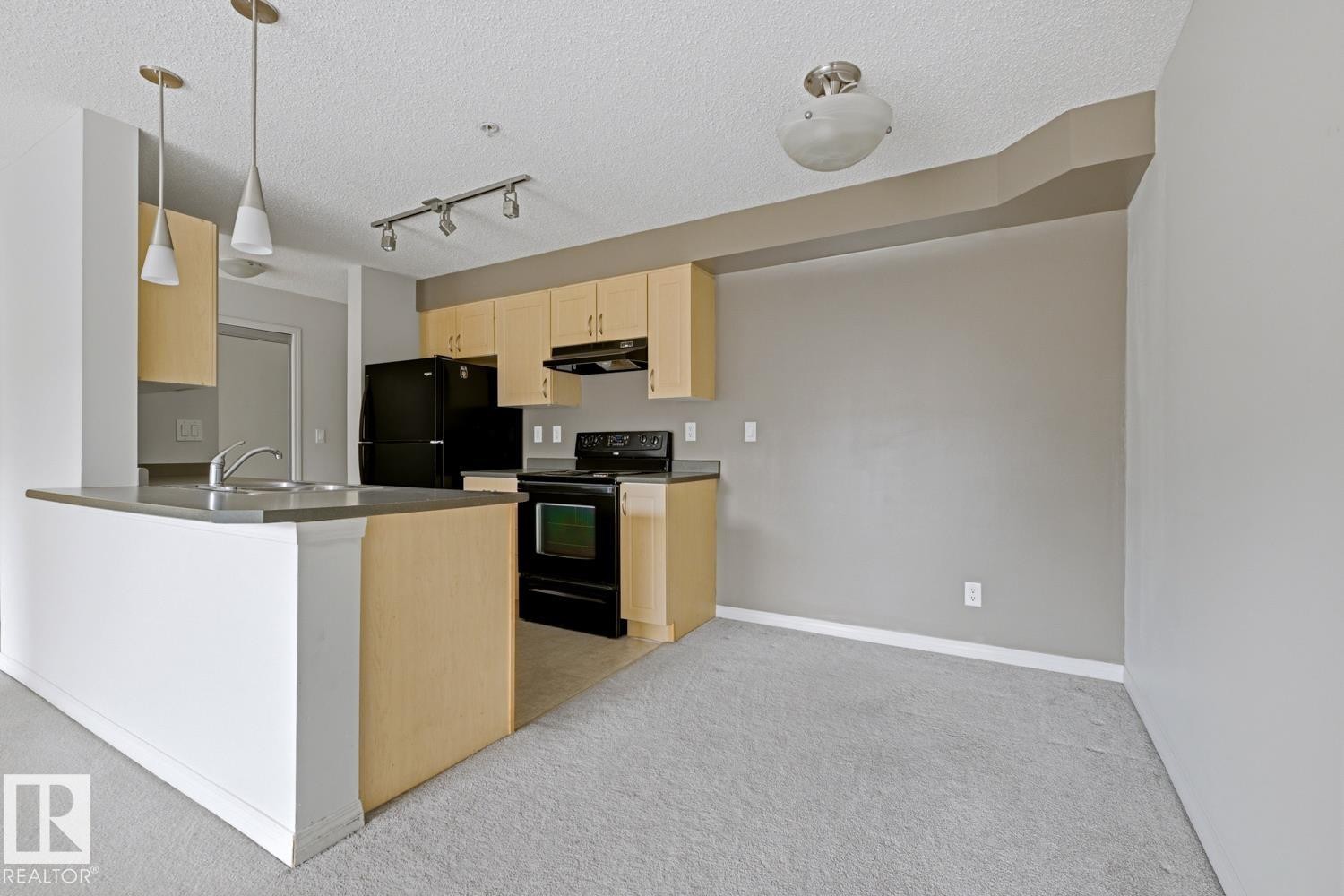 Open-concept kitchen featuring light wood cabinetry, black appliances, a double basin sink, and a peninsula with counter seating - #312 13908 136 St Nw, Edmonton, AB - Indoor Photo Showing Kitchen