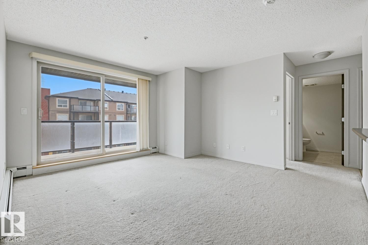 Spacious living area featuring light-toned carpeting and neutral wall paint - #312 13908 136 St Nw, Edmonton, AB - With Exterior