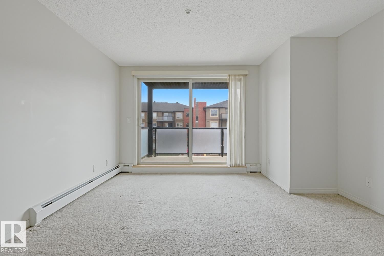 Light-colored wall-to-wall carpeting throughout this room, featuring a sliding glass door leading to a private outdoor balcony with a frosted panel railing - #312 13908 136 St Nw, Edmonton, AB - Indoor Photo Showing Other Room
