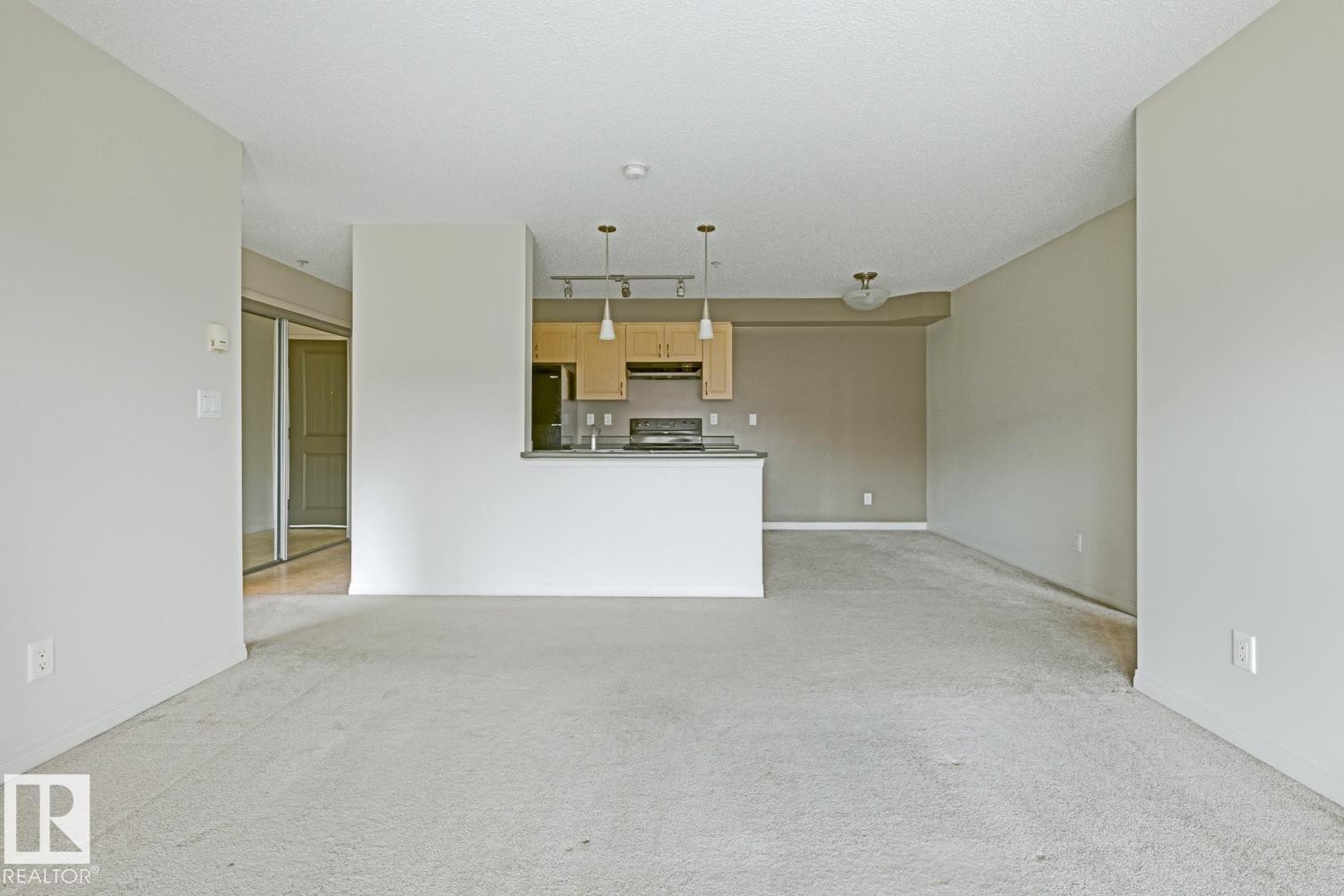 Open concept living area featuring light-toned carpet flooring and a kitchen with light wood cabinetry, a breakfast bar, and pendant lighting - #312 13908 136 St Nw, Edmonton, AB - Indoor Photo Showing Kitchen