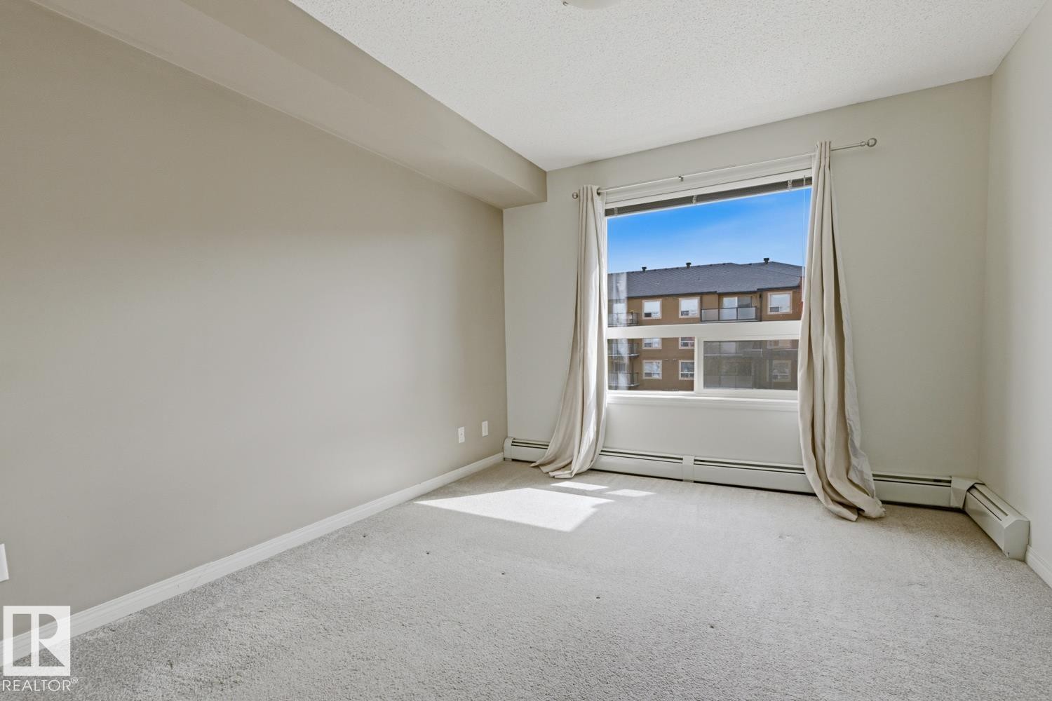 Bright room featuring a large window, light gray carpeting, neutral wall color, and white baseboards - #312 13908 136 St Nw, Edmonton, AB - Indoor Photo Showing Other Room