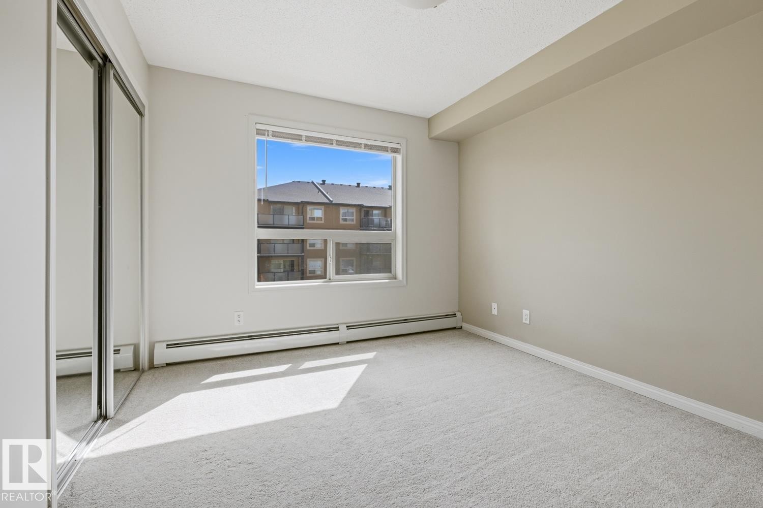 Bright room with a large window, plush carpeting, and mirrored sliding closet doors - #312 13908 136 St Nw, Edmonton, AB - Indoor Photo Showing Other Room