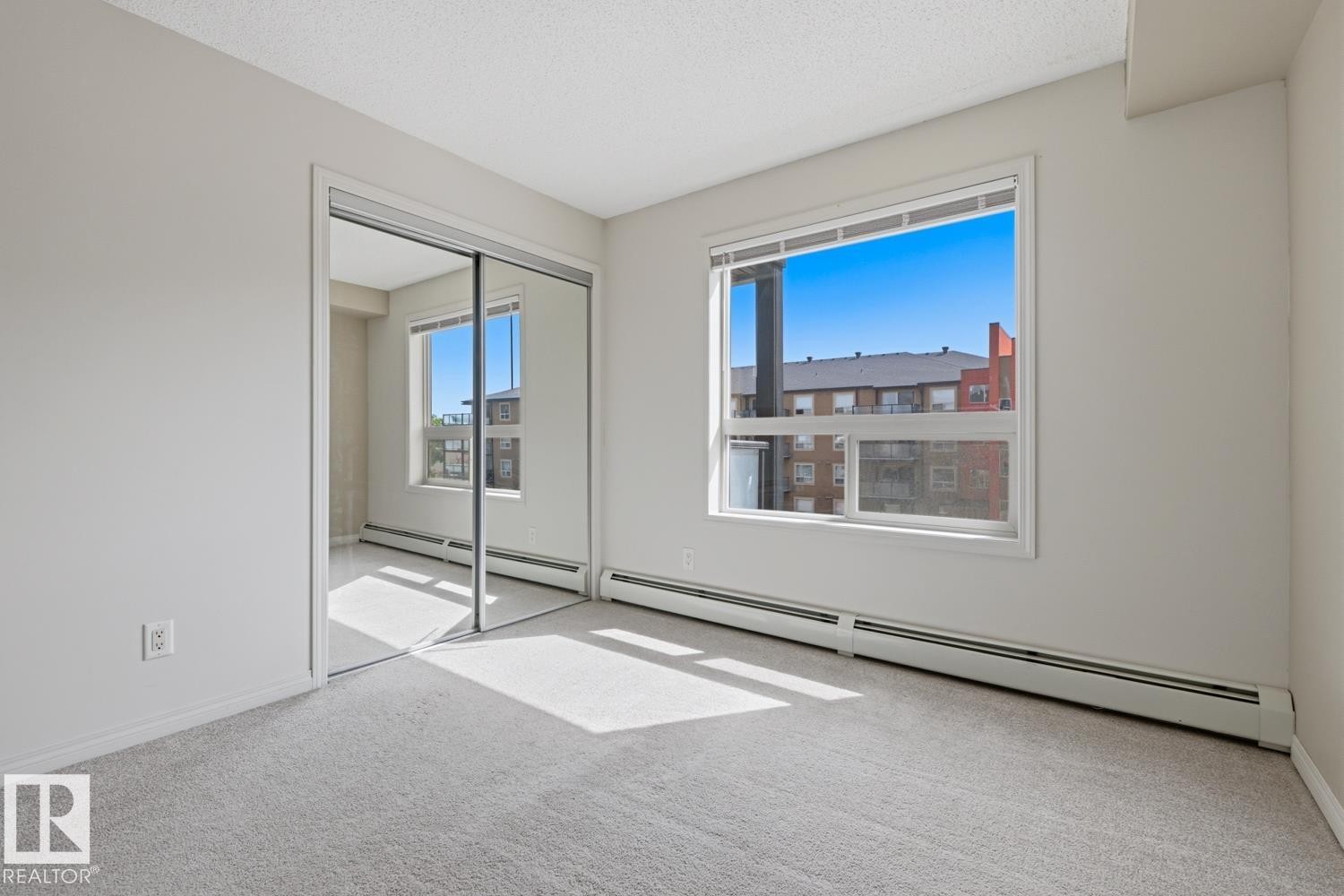 Bright room featuring light grey carpeting, a large window, and mirrored sliding closet doors - #312 13908 136 St Nw, Edmonton, AB - Indoor Photo Showing Other Room