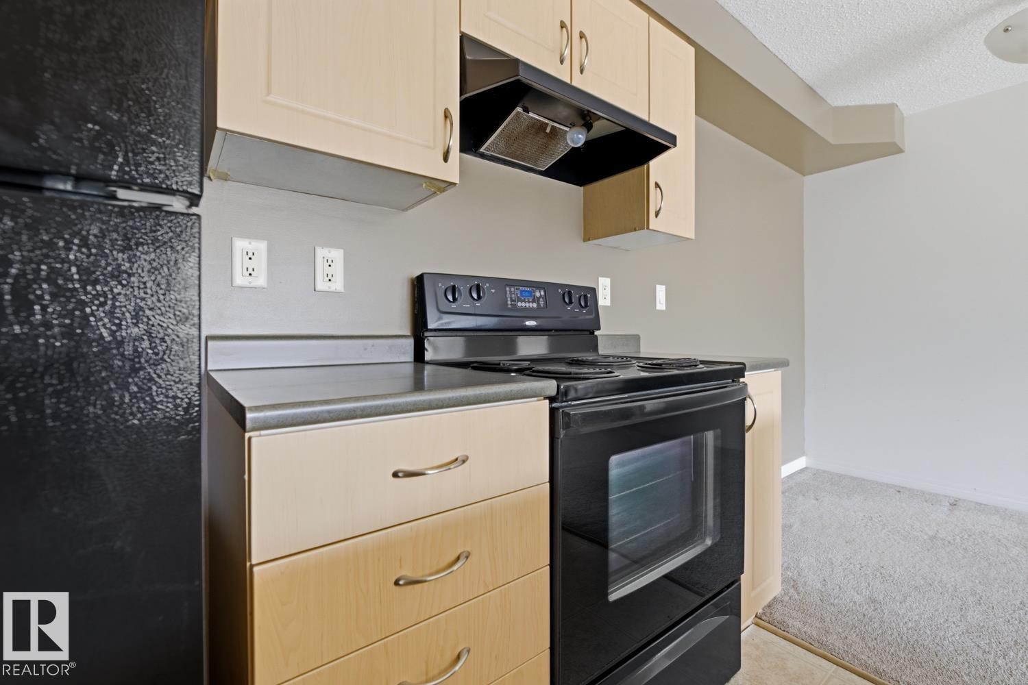 Kitchen area featuring light wood-finish cabinetry, a black electric range, and a black refrigerator - #312 13908 136 St Nw, Edmonton, AB - Indoor Photo Showing Kitchen