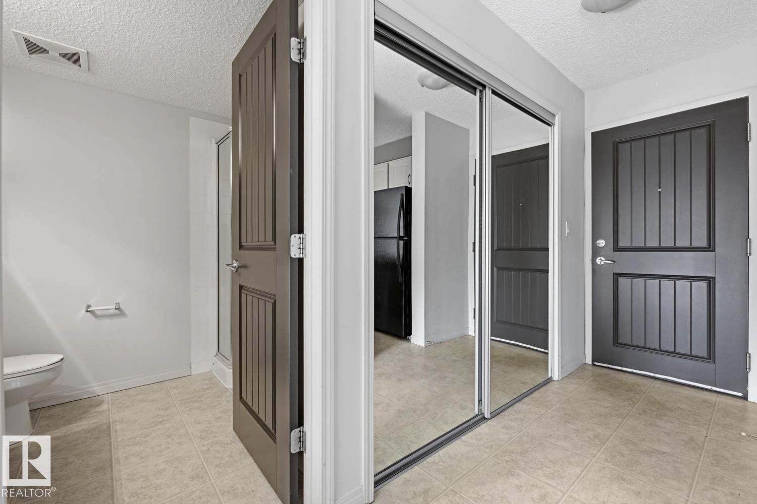 Foyer featuring tile flooring, mirrored sliding closet doors, and a paneled entry door - #312 13908 136 St Nw, Edmonton, AB - Indoor