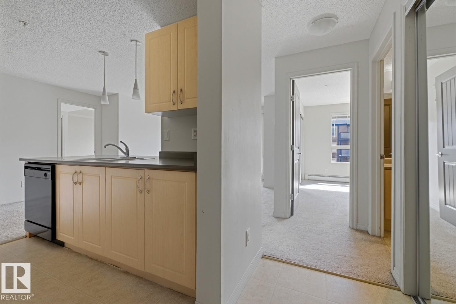 Kitchen featuring light wood-finish cabinetry, dark countertops, a stainless steel sink with a gooseneck faucet, and a built-in black dishwasher - #312 13908 136 St Nw, Edmonton, AB - Indoor