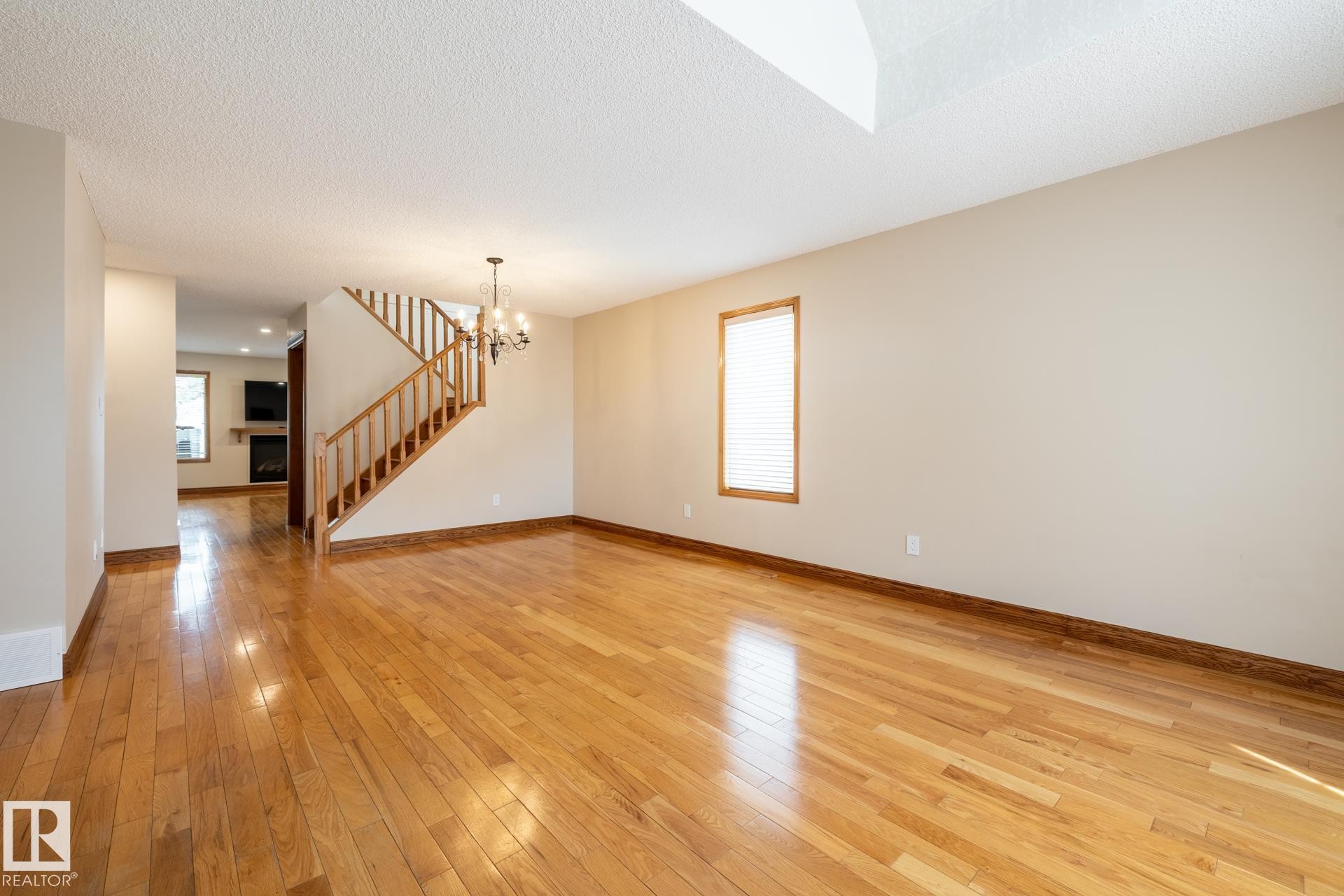 Spacious living area featuring polished wood flooring, a staircase with wood banister and spindles, and a chandelier light fixture - 4632 151 Street, Edmonton, AB - Indoor Photo Showing Other Room