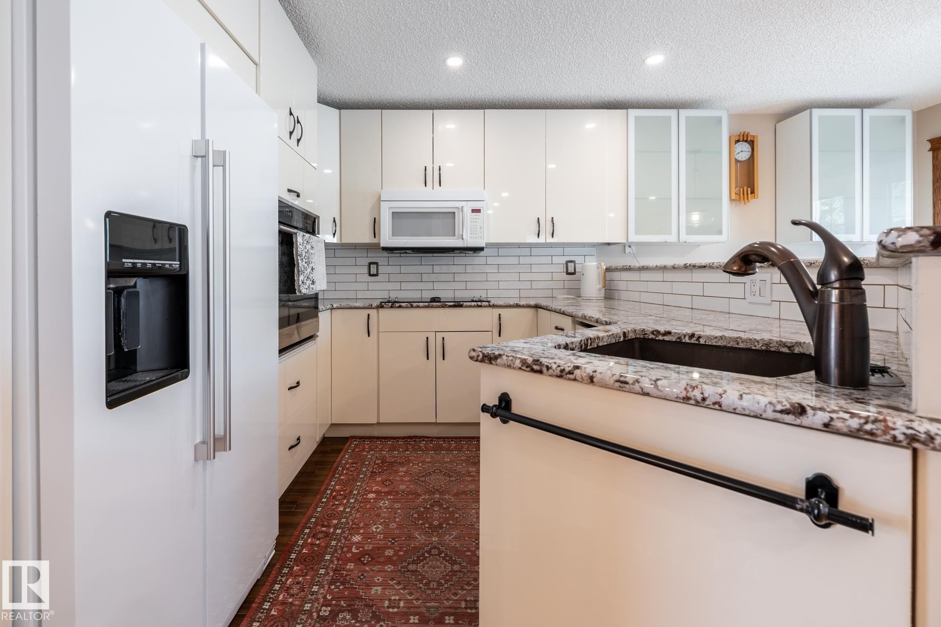 Kitchen featuring a white side-by-side refrigerator, cream-colored cabinetry, light granite countertops, a subway tile backsplash, and recessed lighting - 4632 151 Street, Edmonton, AB - Indoor Photo Showing Kitchen With Upgraded Kitchen