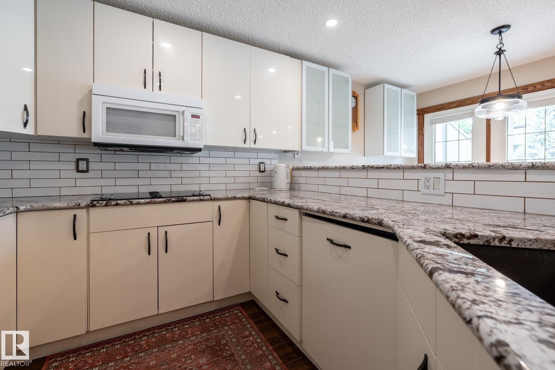 Kitchen featuring light-toned cabinetry with dark hardware, a white subway tile backsplash, and speckled countertops - 4632 151 Street, Edmonton, AB - Indoor Photo Showing Kitchen With Upgraded Kitchen