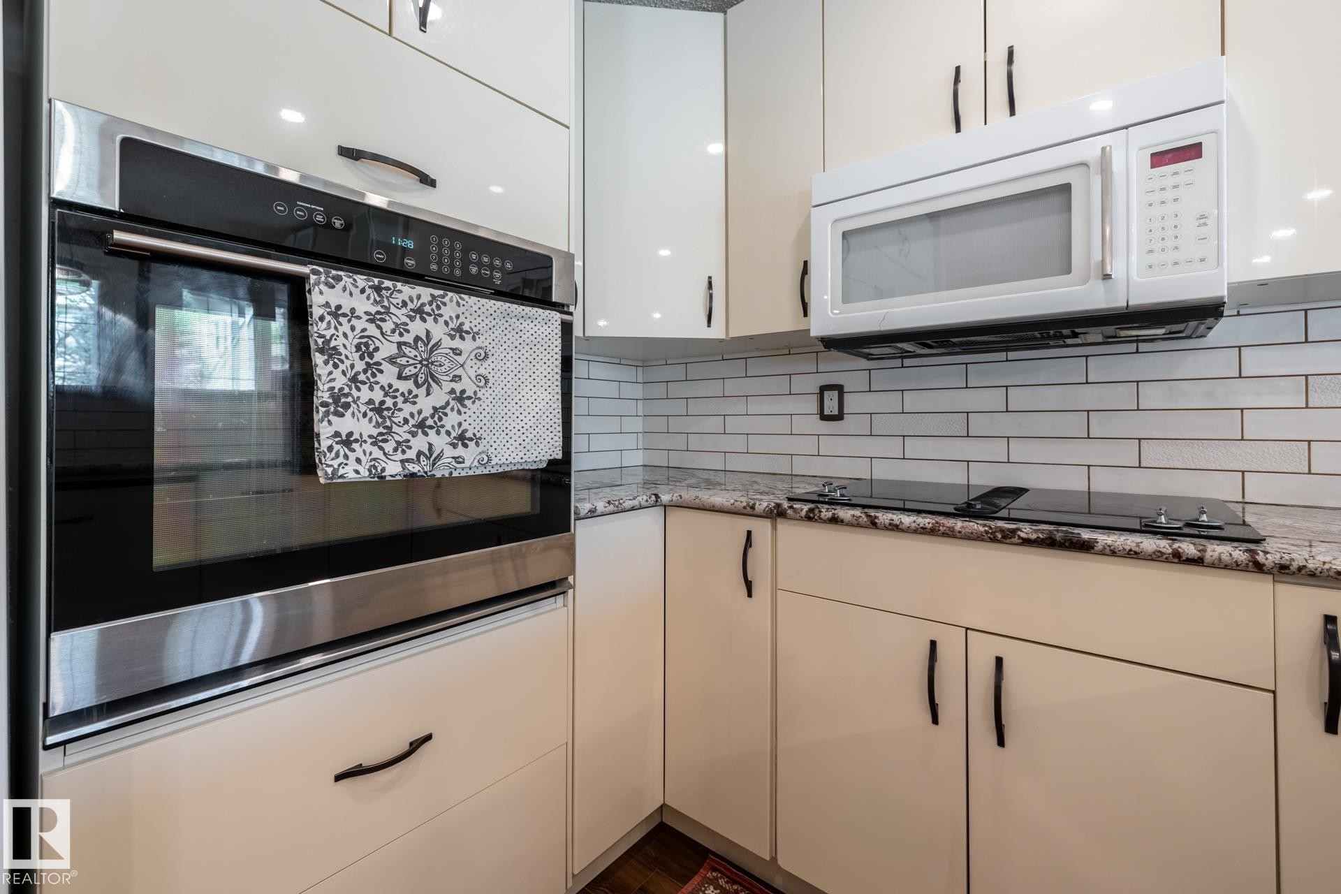 Kitchen featuring a built-in stainless steel oven, white cabinetry with black hardware, white subway tile backsplash, granite countertops, and a black cooktop - 4632 151 Street, Edmonton, AB - Indoor Photo Showing Kitchen With Upgraded Kitchen