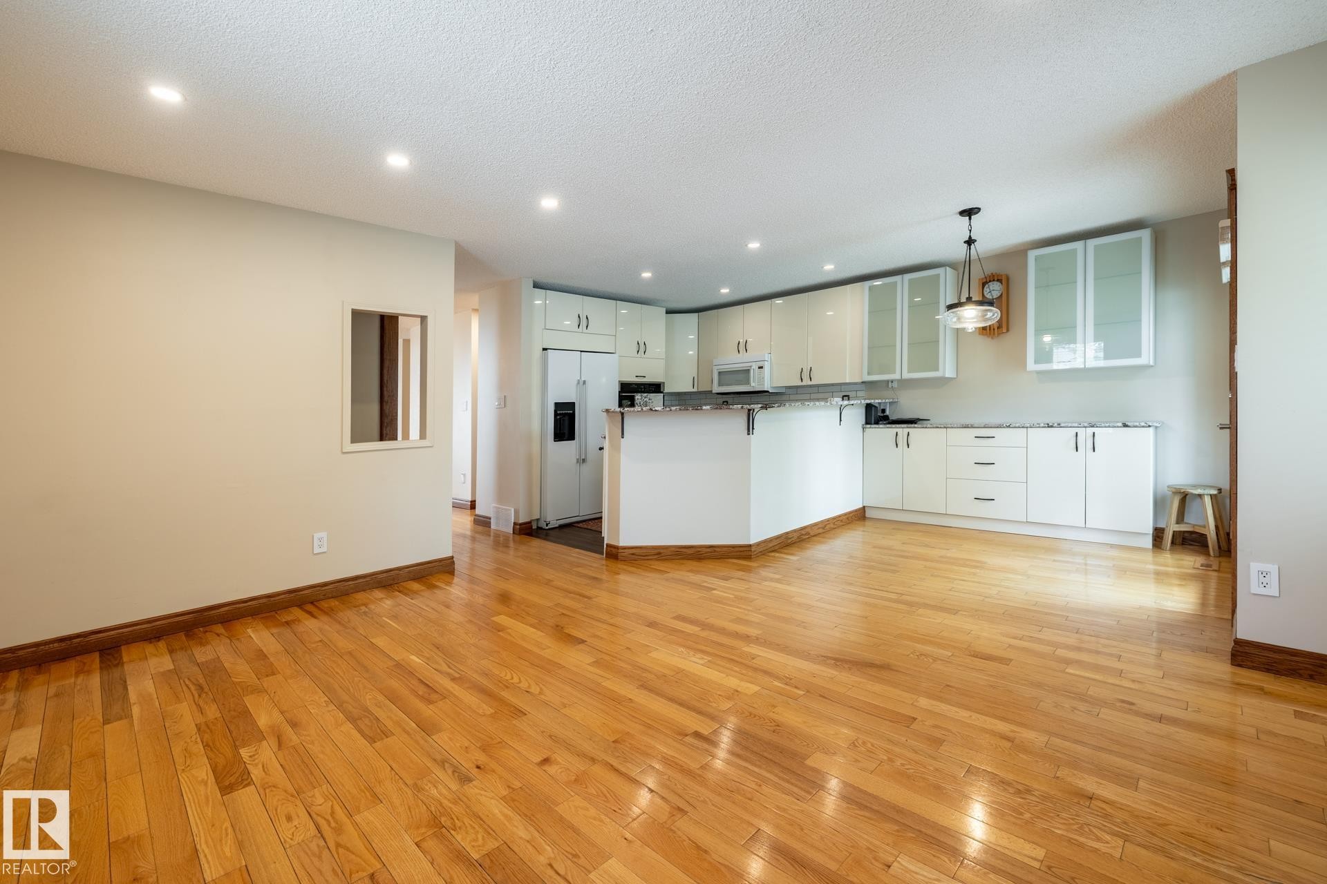 Open-concept kitchen and living area featuring wood-finish flooring, recessed lighting, white cabinetry with glass-front uppers, and stainless steel appliances - 4632 151 Street, Edmonton, AB - Indoor Photo Showing Kitchen