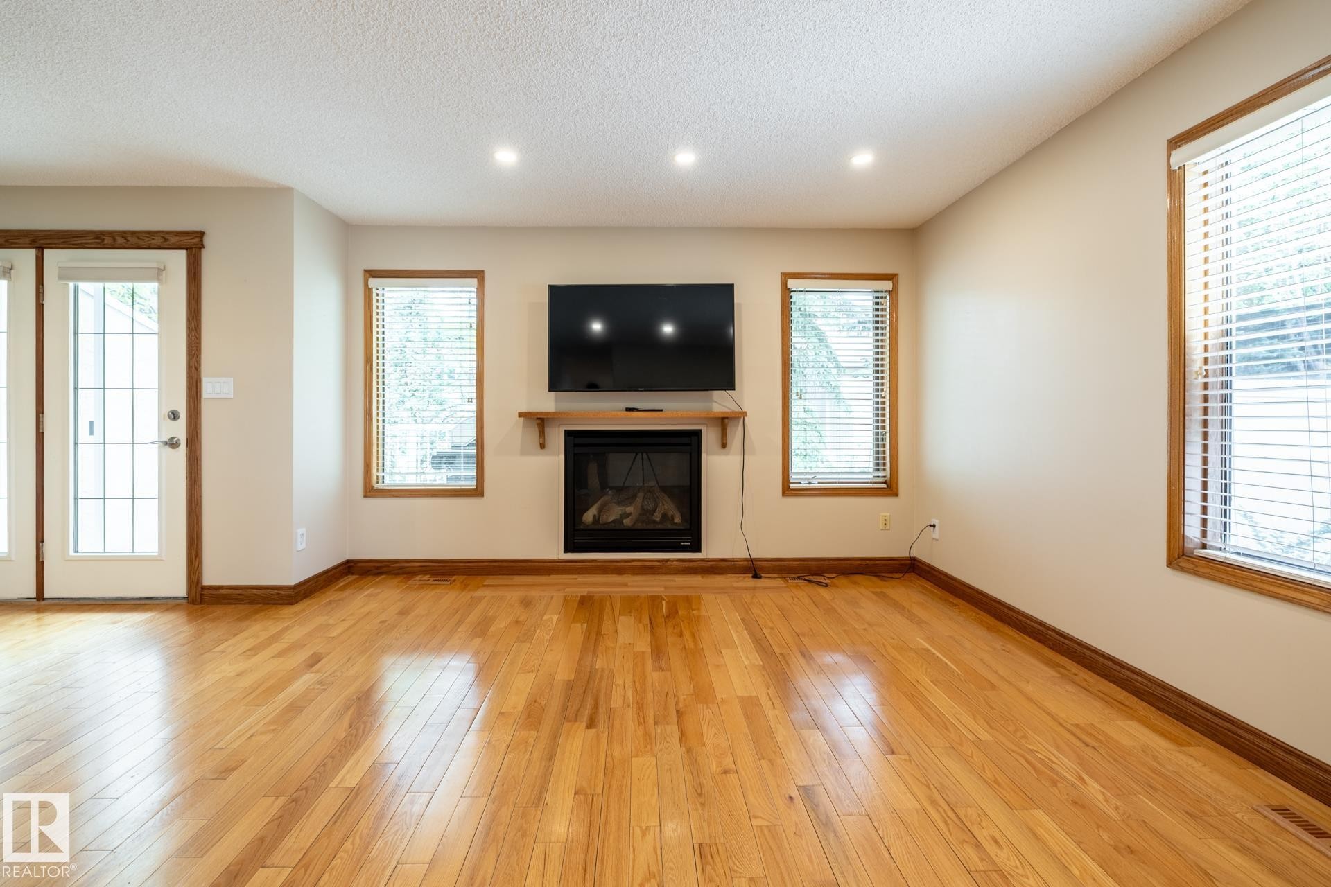 Bright room featuring wood-finish flooring, a built-in fireplace with a wood mantle, recessed lighting, and multiple windows with blinds - 4632 151 Street, Edmonton, AB - Indoor Photo Showing Living Room With Fireplace