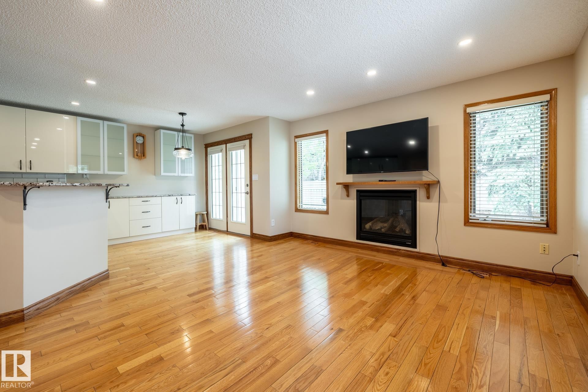 Hardwood flooring throughout a living space featuring a built-in fireplace with a wooden mantel and two windows with blinds - 4632 151 Street, Edmonton, AB - Indoor With Fireplace