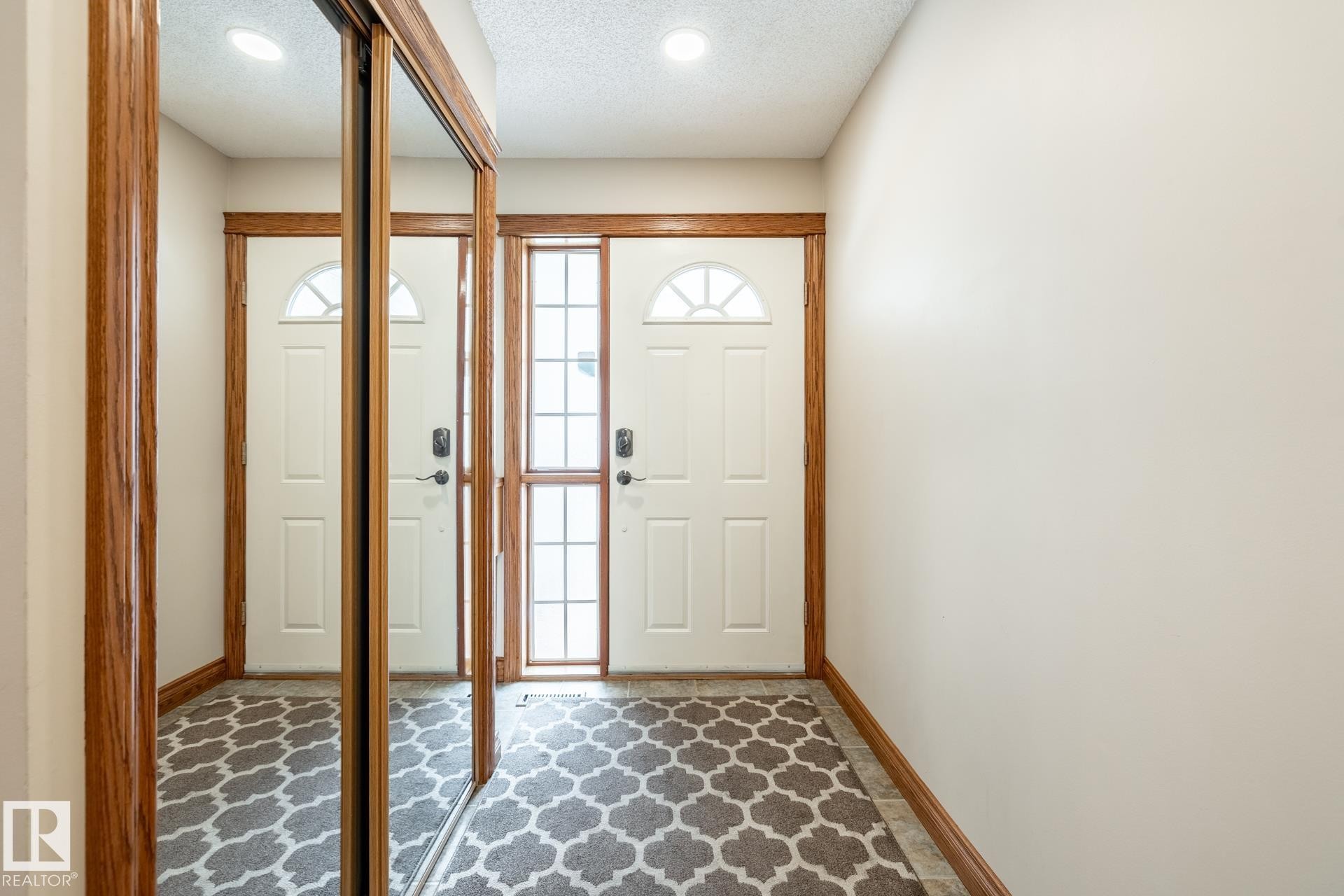 Entryway featuring a sliding mirrored closet door, a white paneled door with an arched window, a storm door with a full-length screen panel, and wood-finish trim - 4632 151 Street, Edmonton, AB - Indoor Photo Showing Other Room