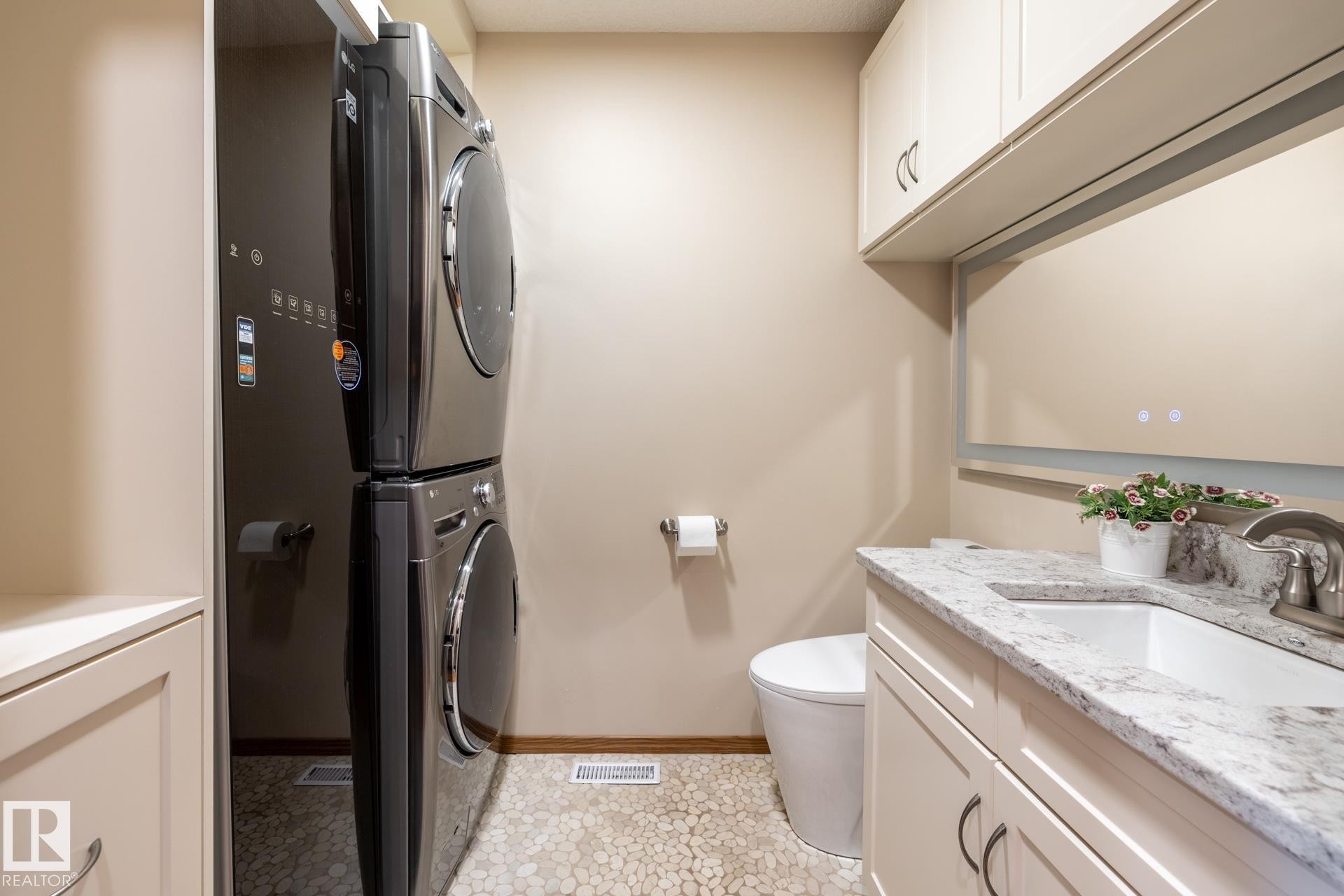 Laundry area with a stacked washer and dryer, complemented by a pebble-finish floor - 4632 151 Street, Edmonton, AB - Indoor Photo Showing Laundry Room