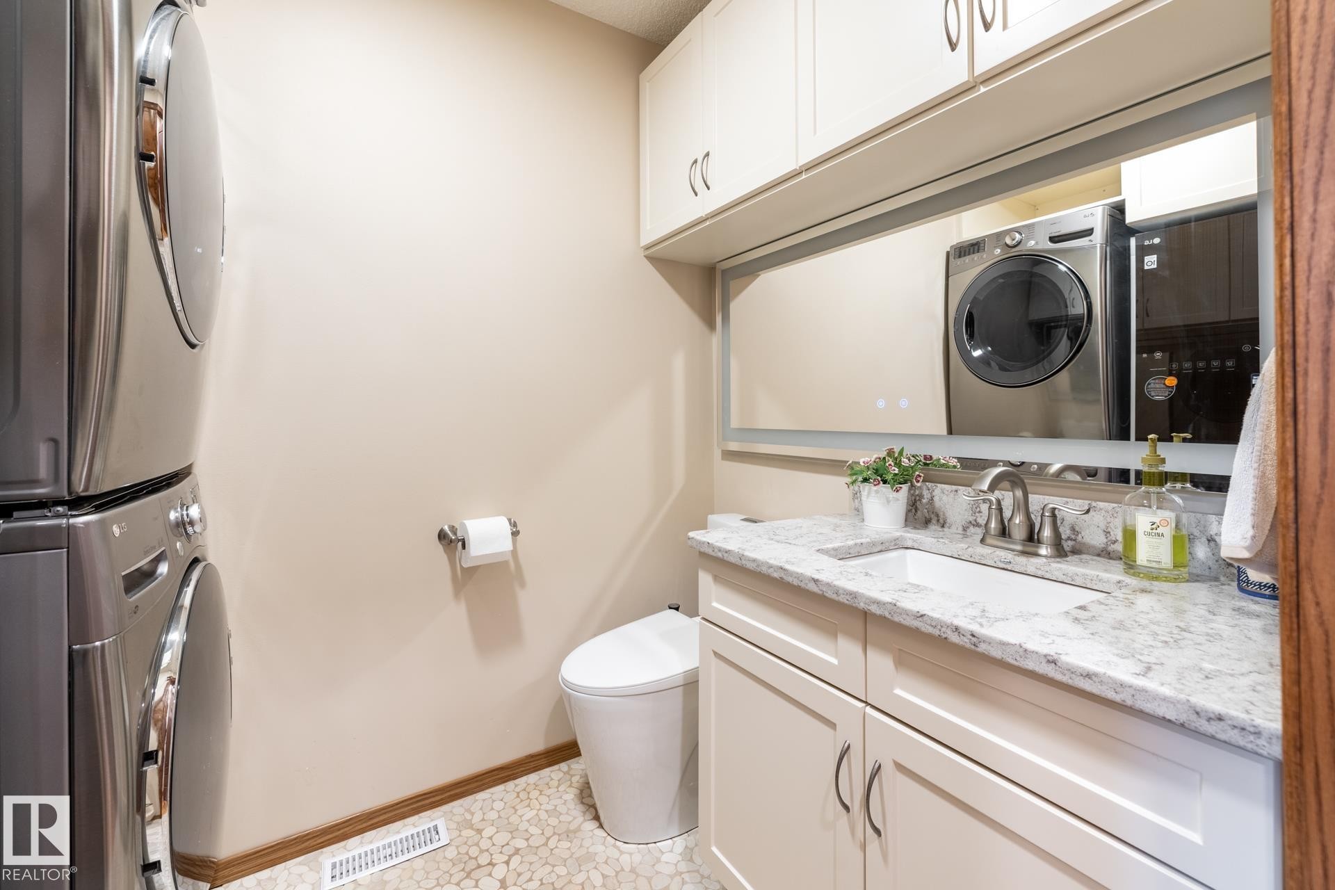 Laundry area featuring stacked appliances, a pebble-finish floor, a compact toilet, a vanity with a light-colored countertop, and integrated upper cabinetry - 4632 151 Street, Edmonton, AB - Indoor Photo Showing Laundry Room