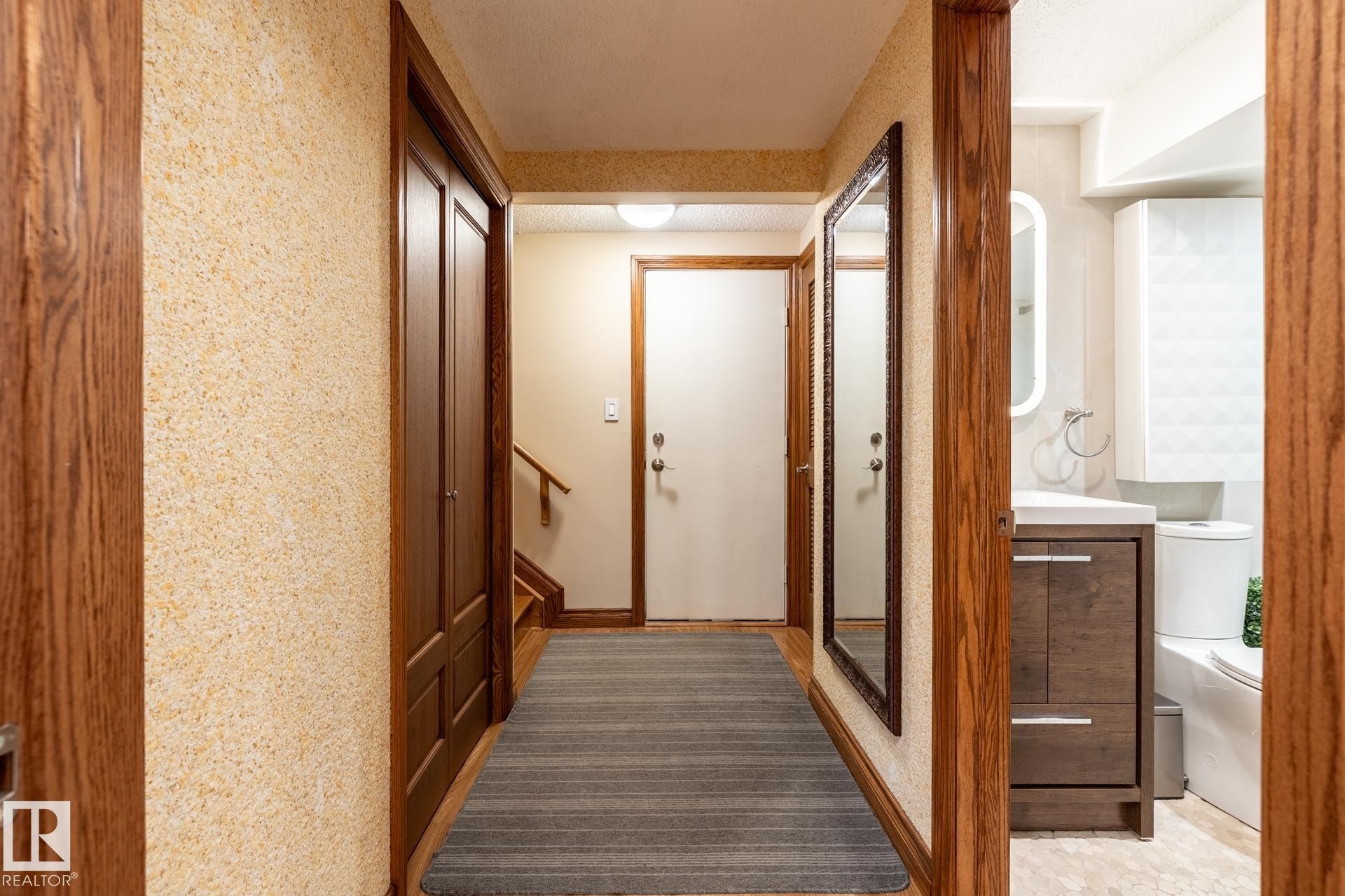 Hallway featuring wood-finish flooring, a full-length mirror, and wood trim accents - 4632 151 Street, Edmonton, AB - Indoor Photo Showing Other Room