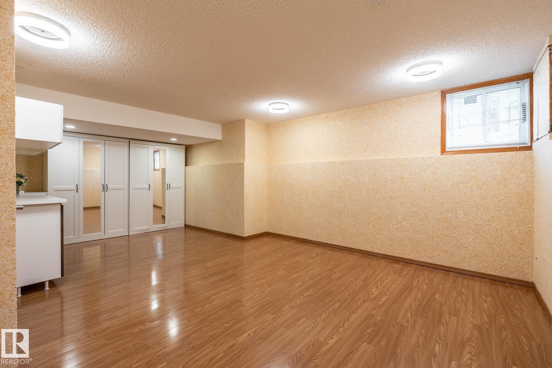 Expansive room featuring wood-finish flooring, recessed lighting, a built-in cabinetry unit with a countertop, and sliding closet doors with mirrored panels - 4632 151 Street, Edmonton, AB - Indoor Photo Showing Other Room