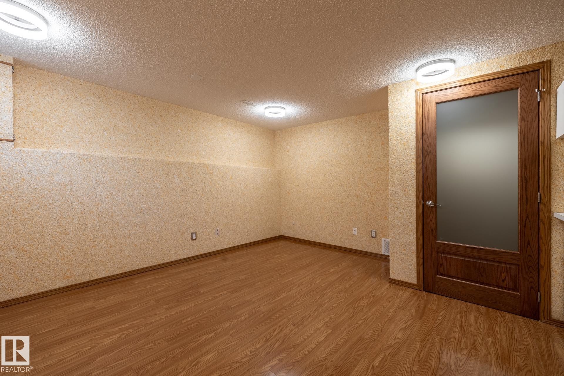 Spacious room featuring wood-finish flooring, textured wall coverings, and contemporary flush-mount lighting - 4632 151 Street, Edmonton, AB - Indoor Photo Showing Other Room