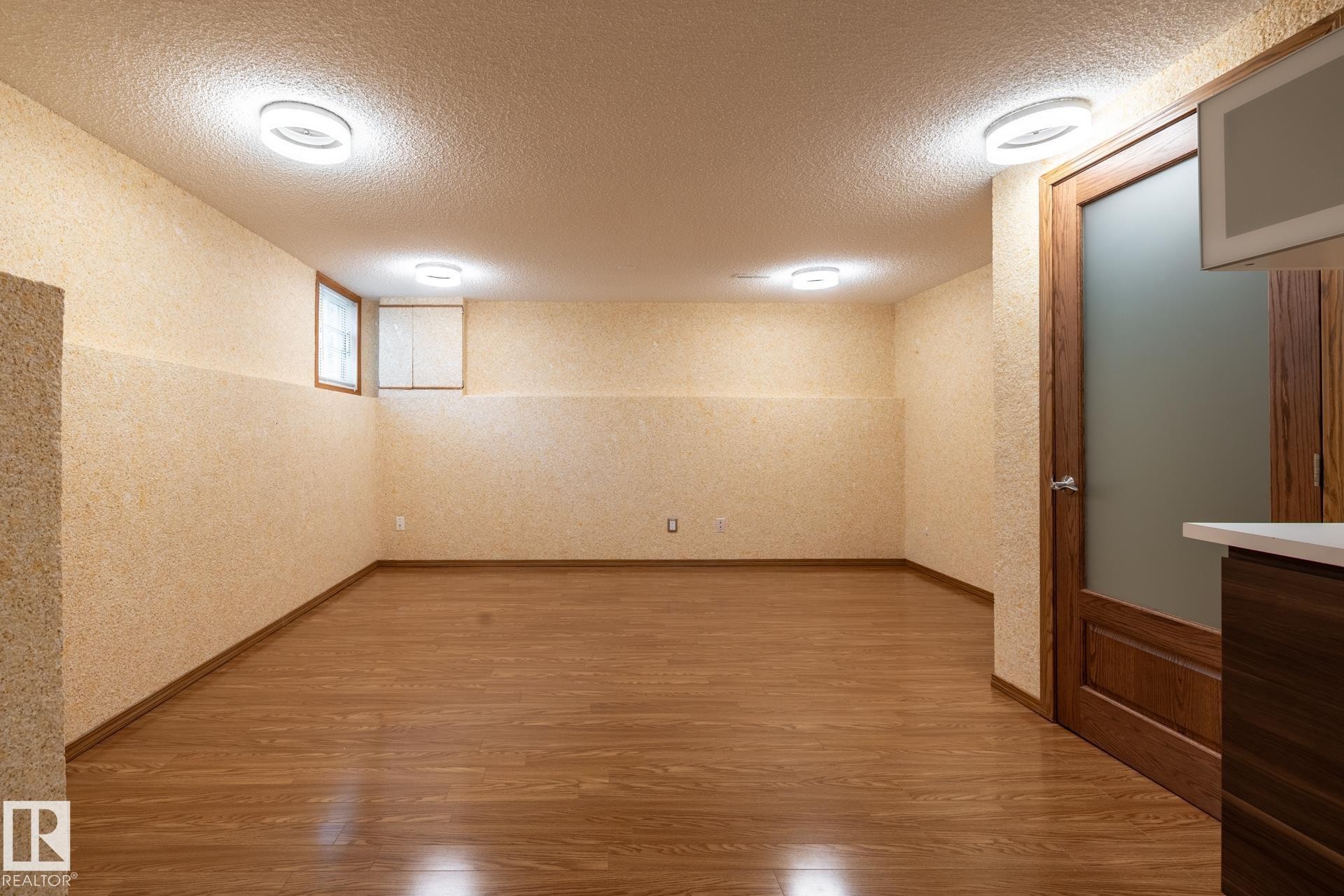 Spacious room featuring wood-finish flooring, textured wall finishes, and multiple flush-mount ceiling lights - 4632 151 Street, Edmonton, AB - Indoor Photo Showing Other Room