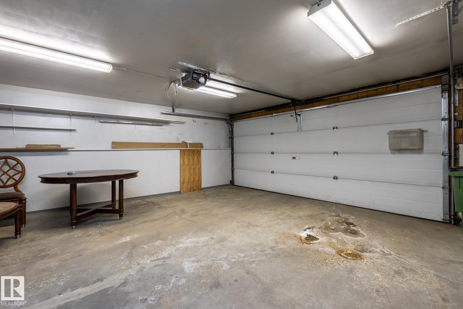 Spacious garage featuring a concrete floor, overhead fluorescent lighting, and a white paneled garage door - 4632 151 Street, Edmonton, AB - Indoor Photo Showing Garage