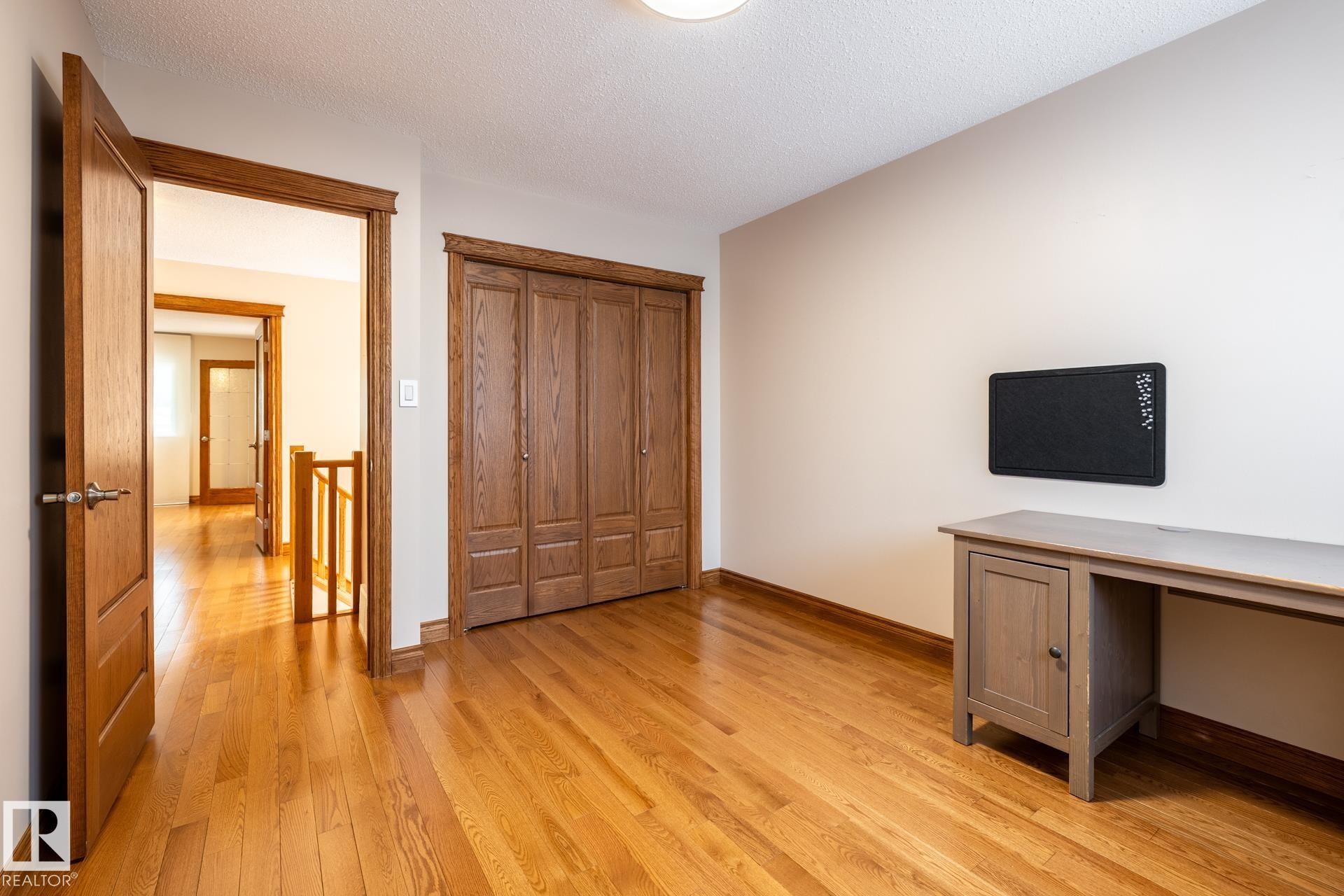 Room featuring hardwood flooring and a built-in closet with wood-panel doors - 4632 151 Street, Edmonton, AB - Indoor