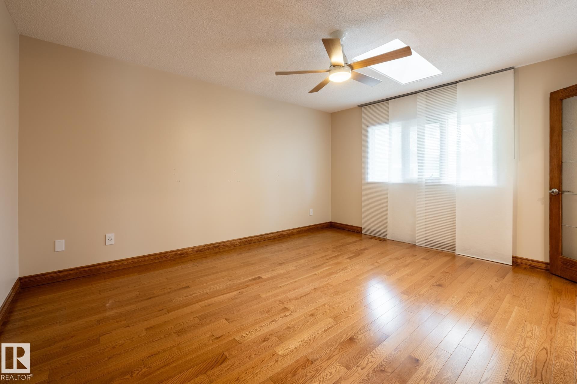 Hardwood flooring throughout featuring a ceiling fan, a skylight, and a window with sheer panel blinds - 4632 151 Street, Edmonton, AB - Indoor Photo Showing Other Room