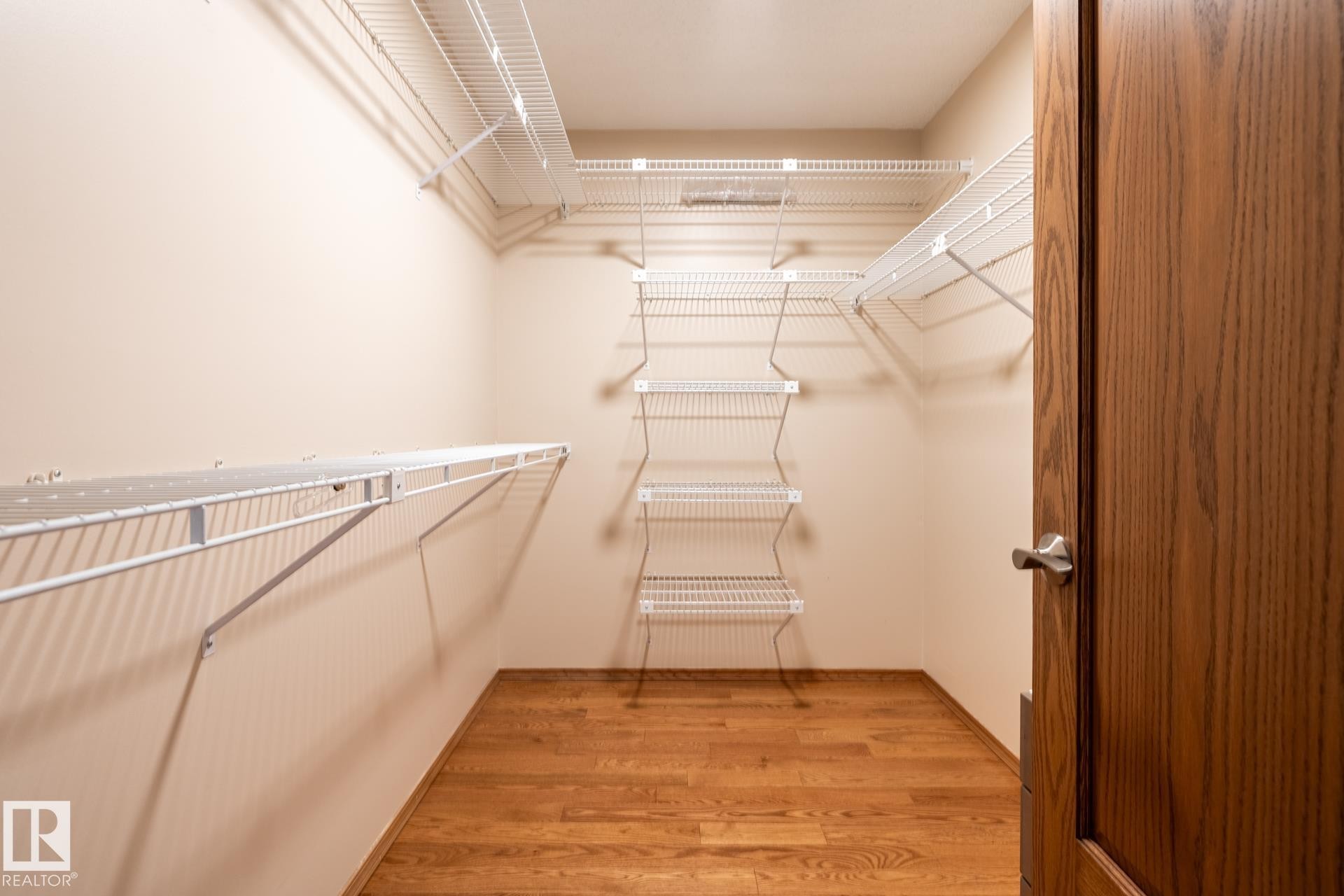 Walk-in closet featuring wire shelving, multiple storage levels, wood-finish flooring, and a paneled wood door with brushed nickel hardware - 4632 151 Street, Edmonton, AB - Indoor With Storage