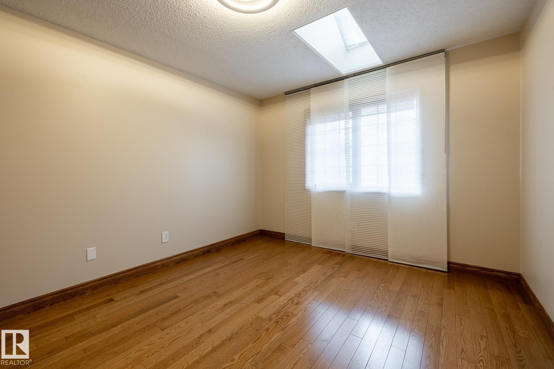 Room featuring wood-finish flooring, a skylight, and a window with blinds and sheer panel coverings - 4632 151 Street, Edmonton, AB - Indoor Photo Showing Other Room