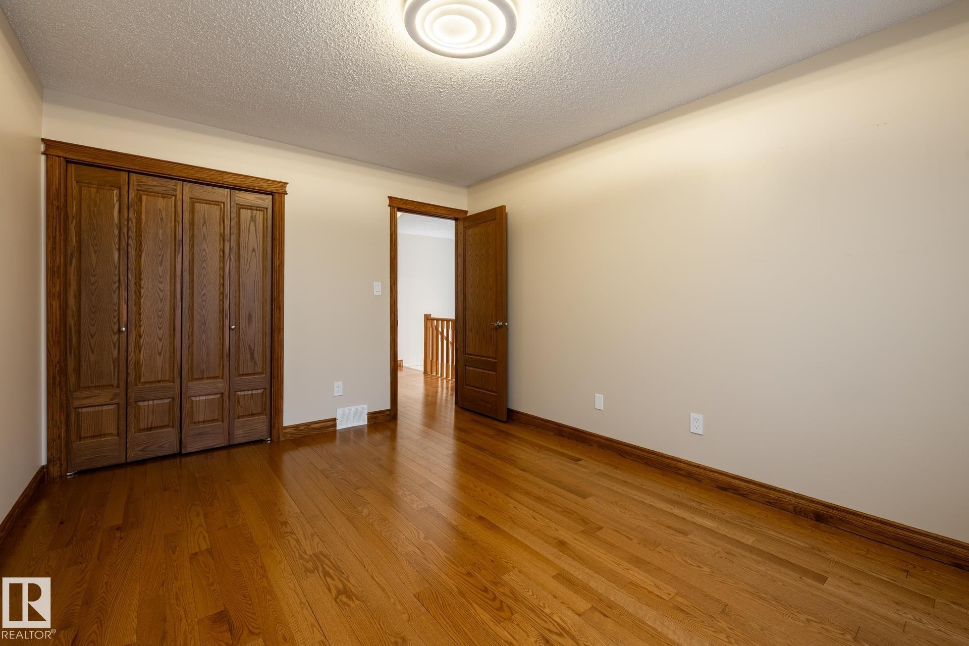 Hardwood flooring extending throughout, bi-fold closet doors, and wood-finish trim - 4632 151 Street, Edmonton, AB - Indoor Photo Showing Other Room