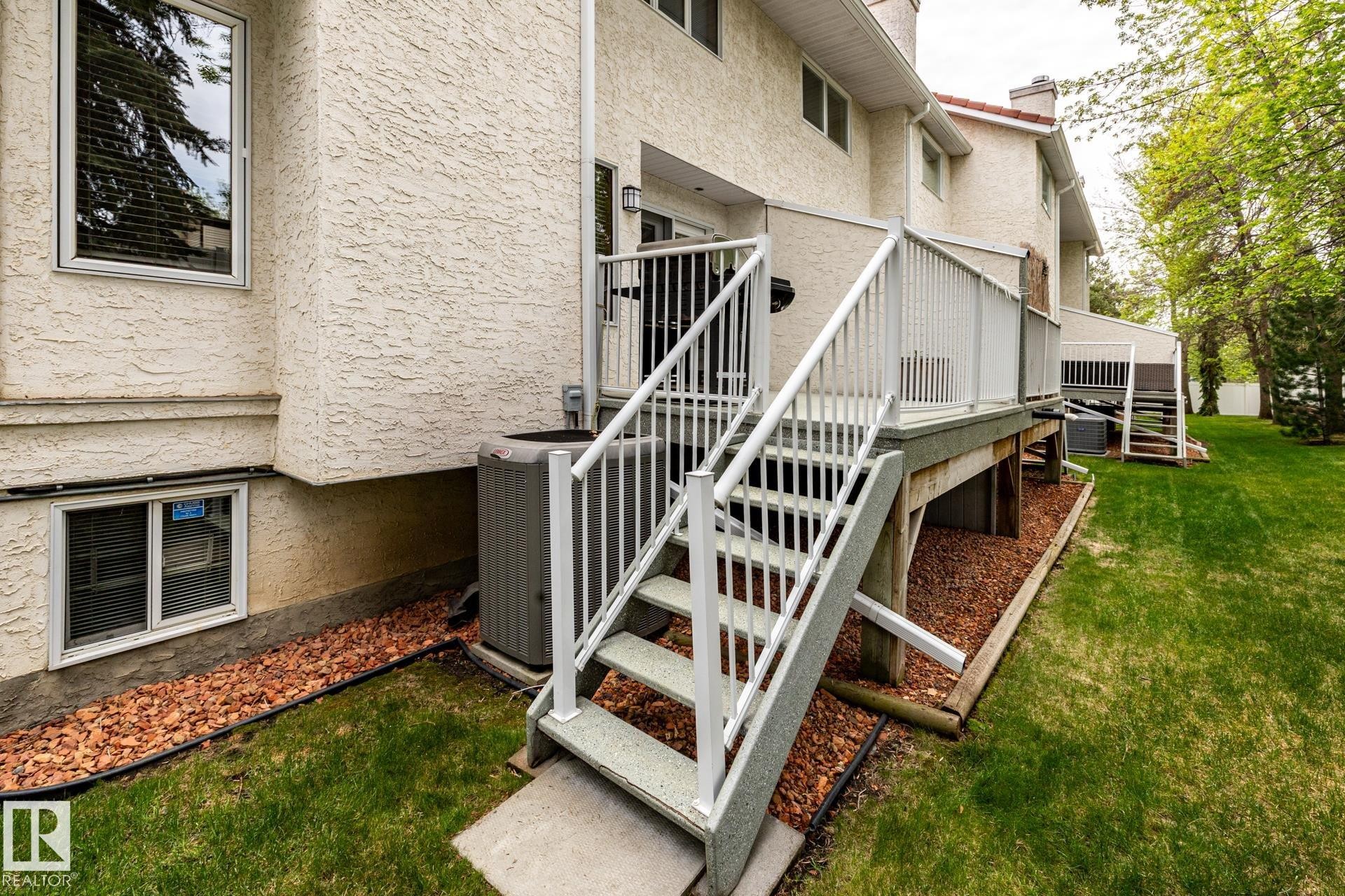 Rear exterior featuring a multi-level deck with white railings, a concrete patio, and a manicured lawn - 4632 151 Street, Edmonton, AB - Outdoor With Exterior