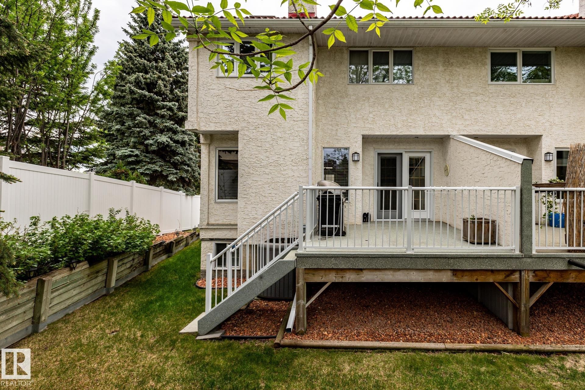 Rear exterior featuring a multi-level deck with white railings, a stucco finish facade, and mature perimeter trees - 4632 151 Street, Edmonton, AB - Outdoor With Deck Patio Veranda