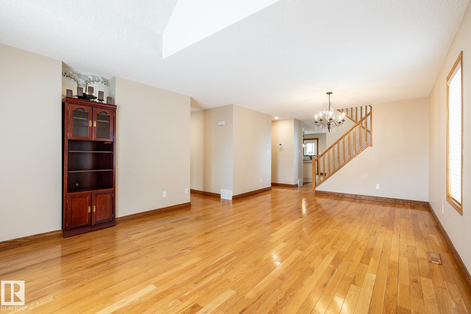 Expansive living area featuring wood-finish flooring, a chandelier, a staircase with wood railings, a window with blinds, and neutral wall tones - 4632 151 Street, Edmonton, AB - Indoor Photo Showing Other Room