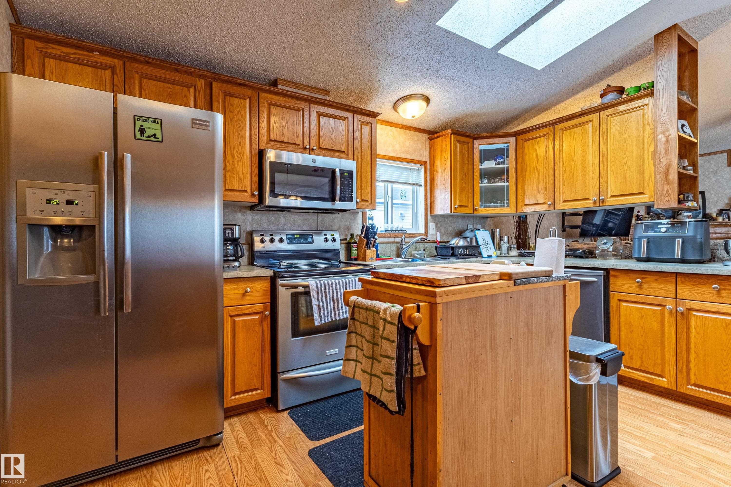 Kitchen featuring wood cabinetry, stainless steel appliances, a wood-finish flooring, and overhead skylight - 1529 Range Road 272 Rural Parkland County, Alberta, Rural Parkland County, AB - Indoor Photo Showing Kitchen With Stainless Steel Kitchen