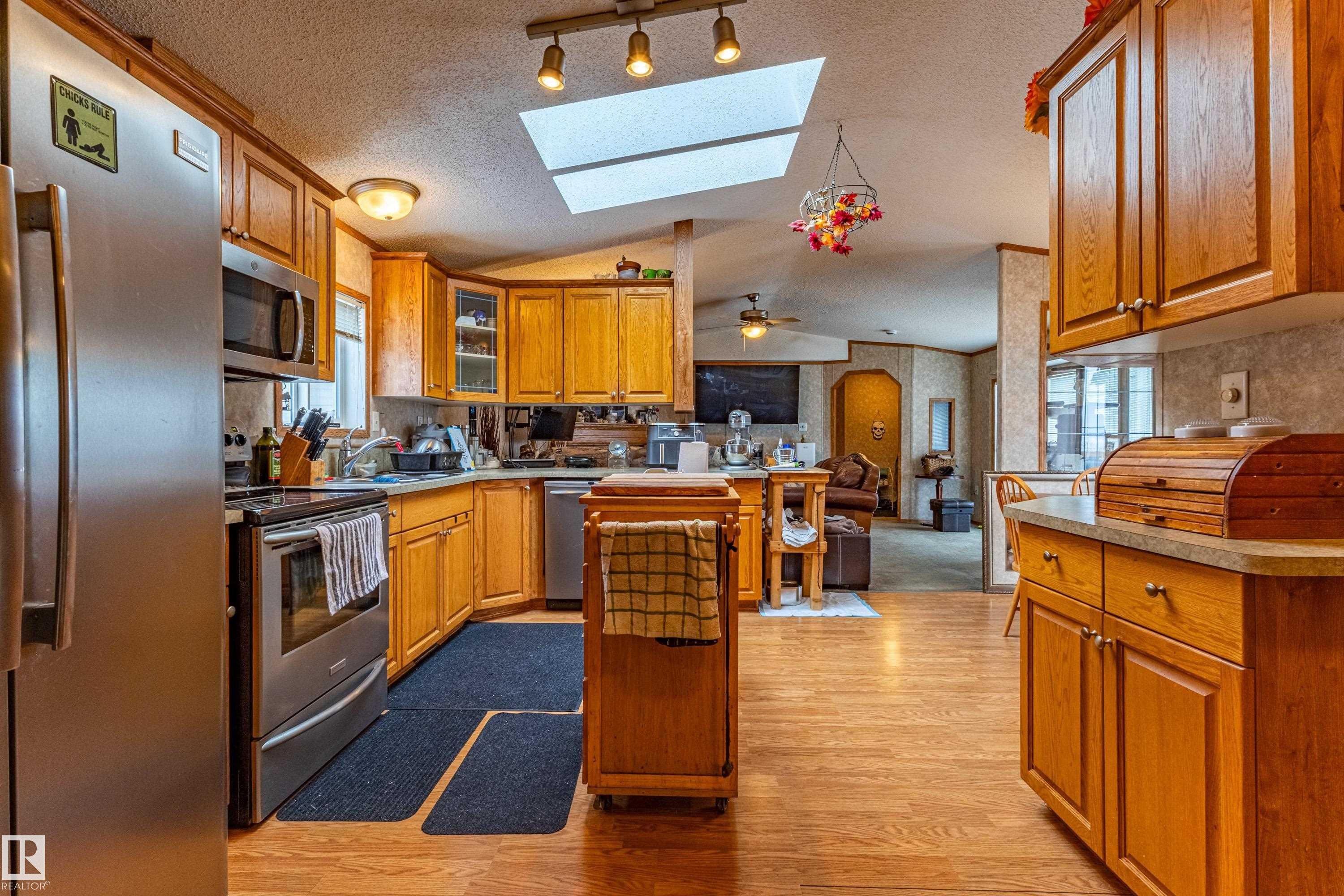 Kitchen featuring wood-finish flooring, warm-toned cabinetry, stainless steel appliances, and a skylight - 1529 Range Road 272 Rural Parkland County, Alberta, Rural Parkland County, AB - Indoor Photo Showing Kitchen