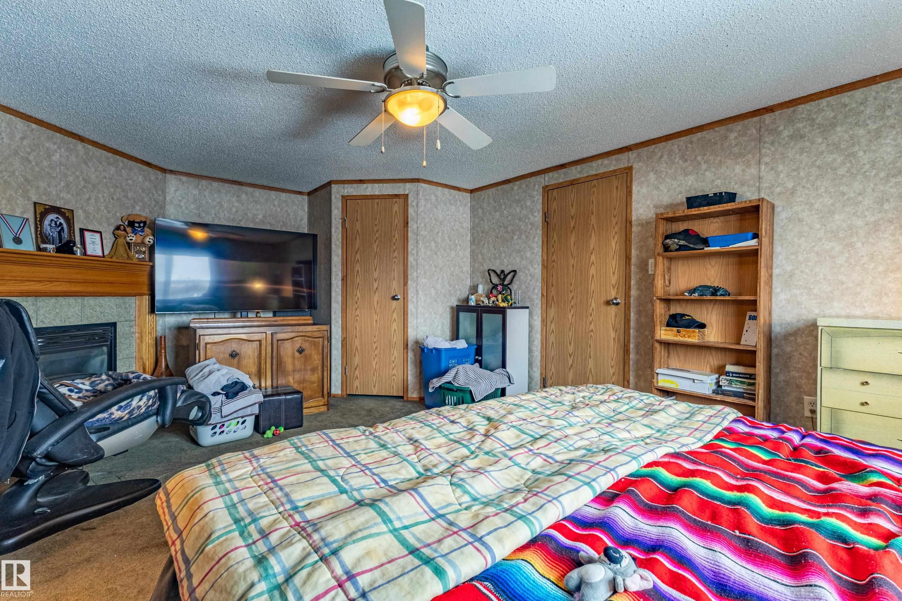 Interior space featuring a ceiling fan with integrated lighting, wood-finish doors, textured wall paneling, and a built-in fireplace with a wood mantle - 1529 Range Road 272 Rural Parkland County, Alberta, Rural Parkland County, AB - Indoor Photo Showing Bedroom