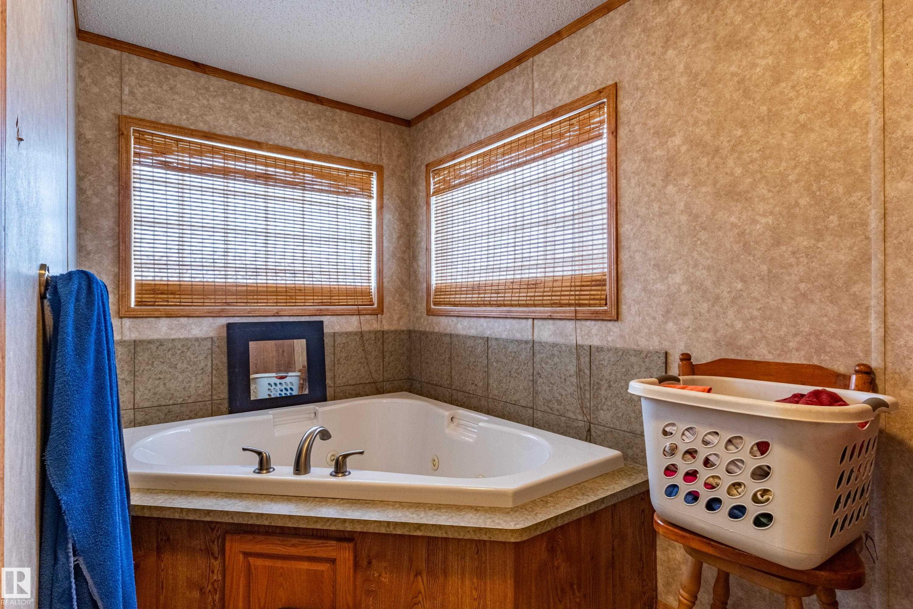 Corner soaking tub with deck-mounted fixtures, two windows with wood blinds, wood-finish cabinetry, and tiled wainscoting - 1529 Range Road 272 Rural Parkland County, Alberta, Rural Parkland County, AB - Indoor Photo Showing Bathroom