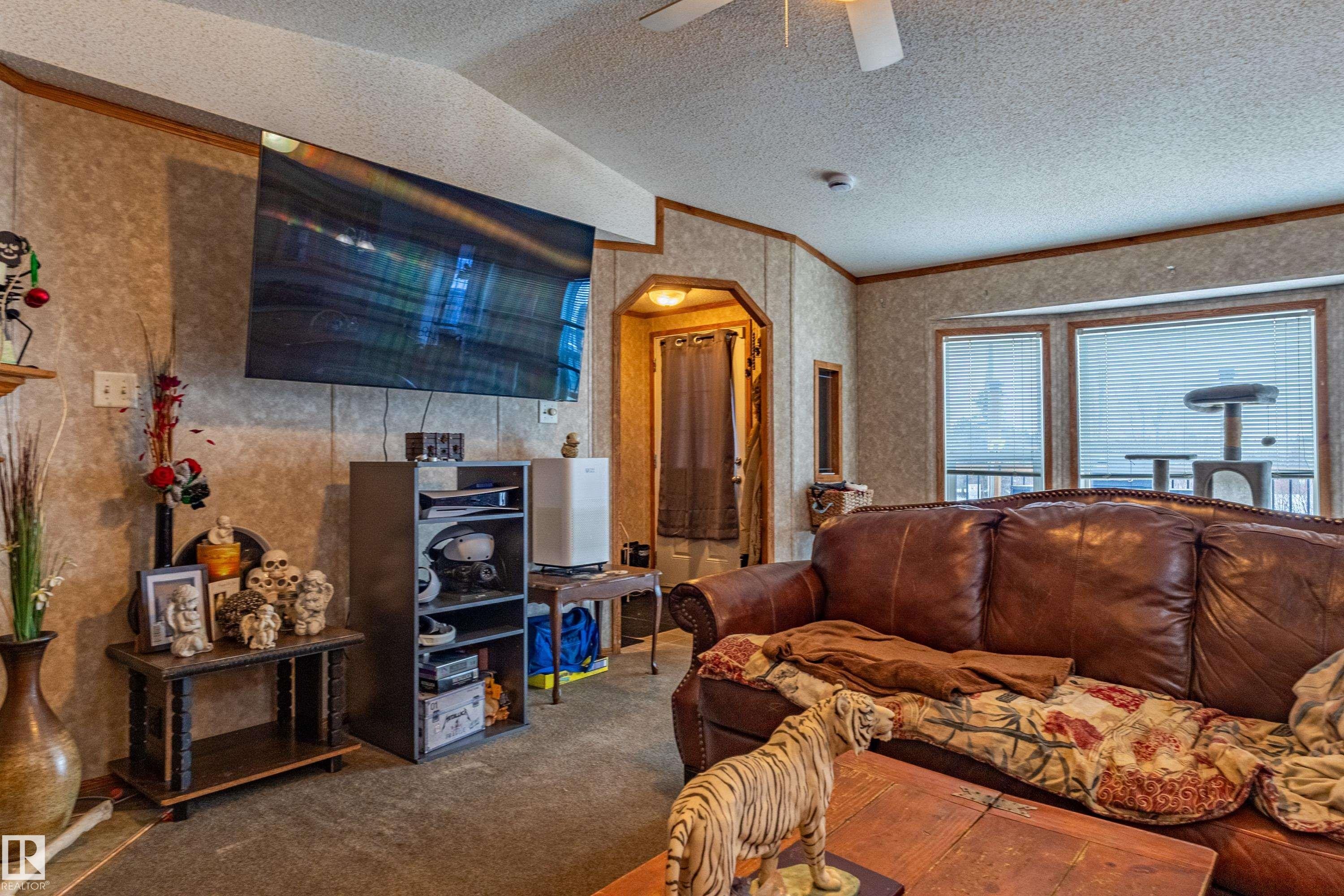 Living area featuring textured wall finishes, wood-finish trim, a mounted television, and a ceiling fan - 1529 Range Road 272 Rural Parkland County, Alberta, Rural Parkland County, AB - Indoor Photo Showing Living Room