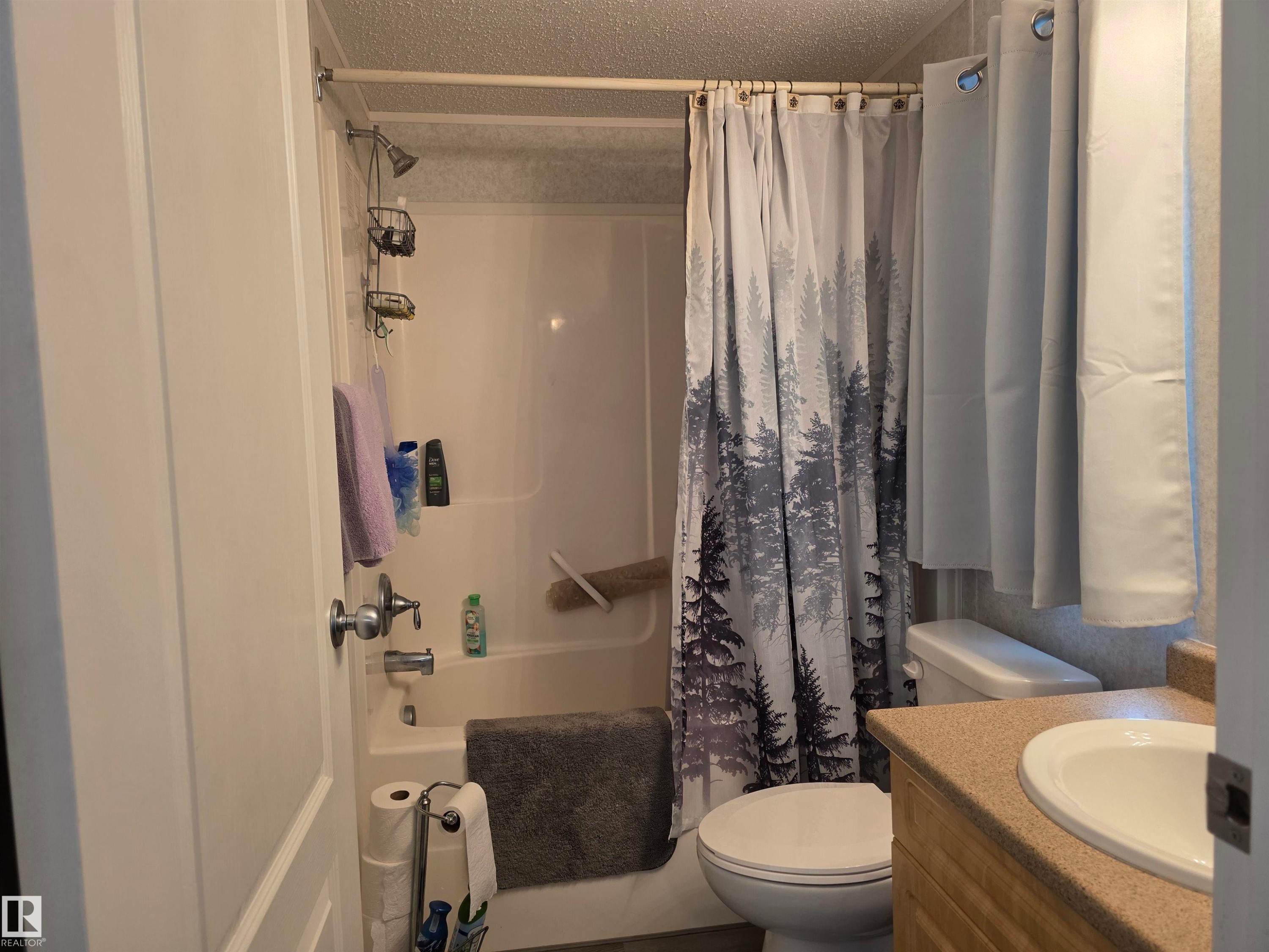 Full bathroom featuring a shower-tub combination, a vanity with an integrated sink, and a commode - 5012 53 Ave, Breton, AB