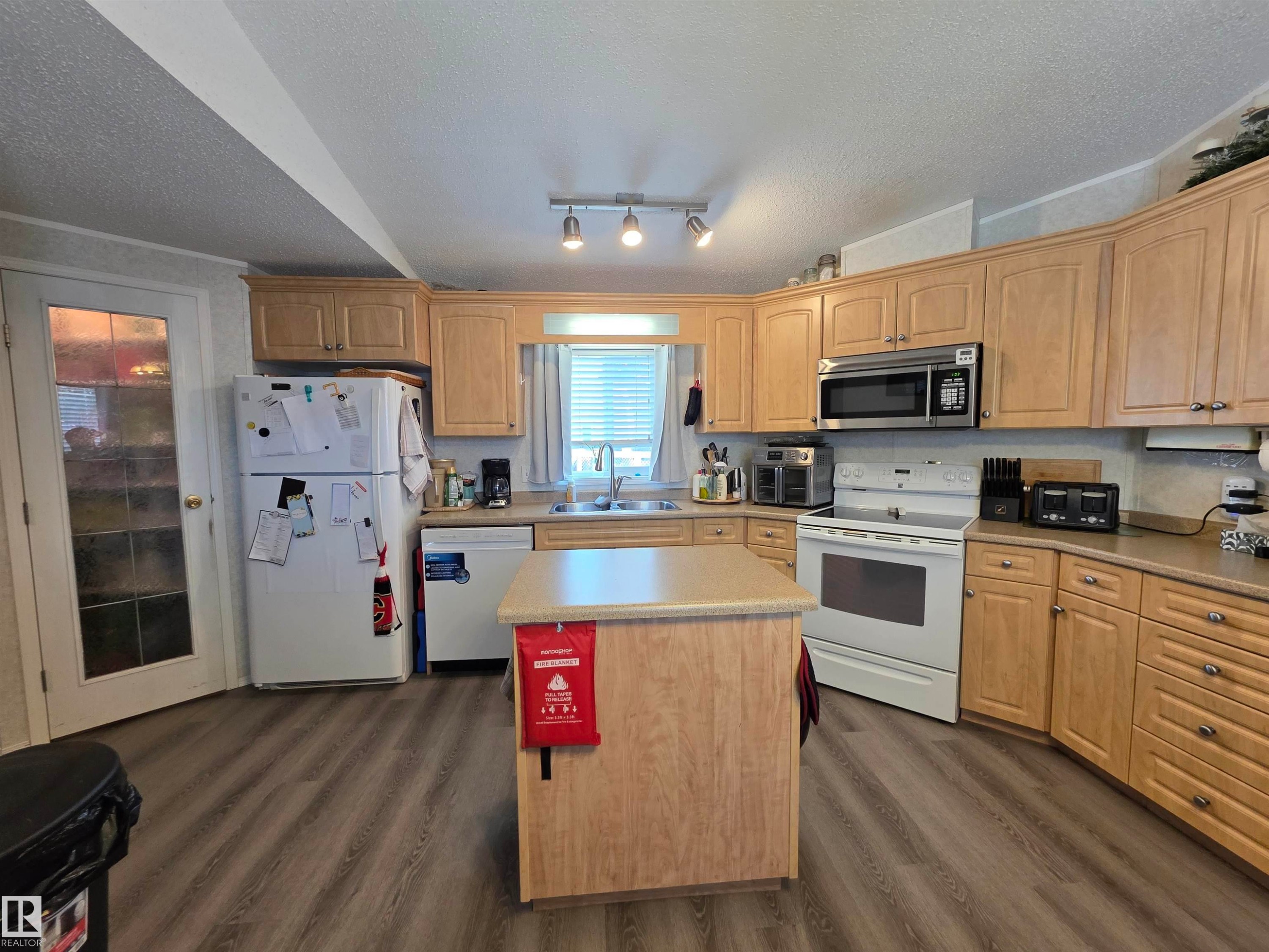 Kitchen featuring light wood-finish cabinetry, a central island WITH POWER, laminate countertops, and VINYL PLANK flooring, corner walk in pantry - 5012 53 Ave, Breton, AB