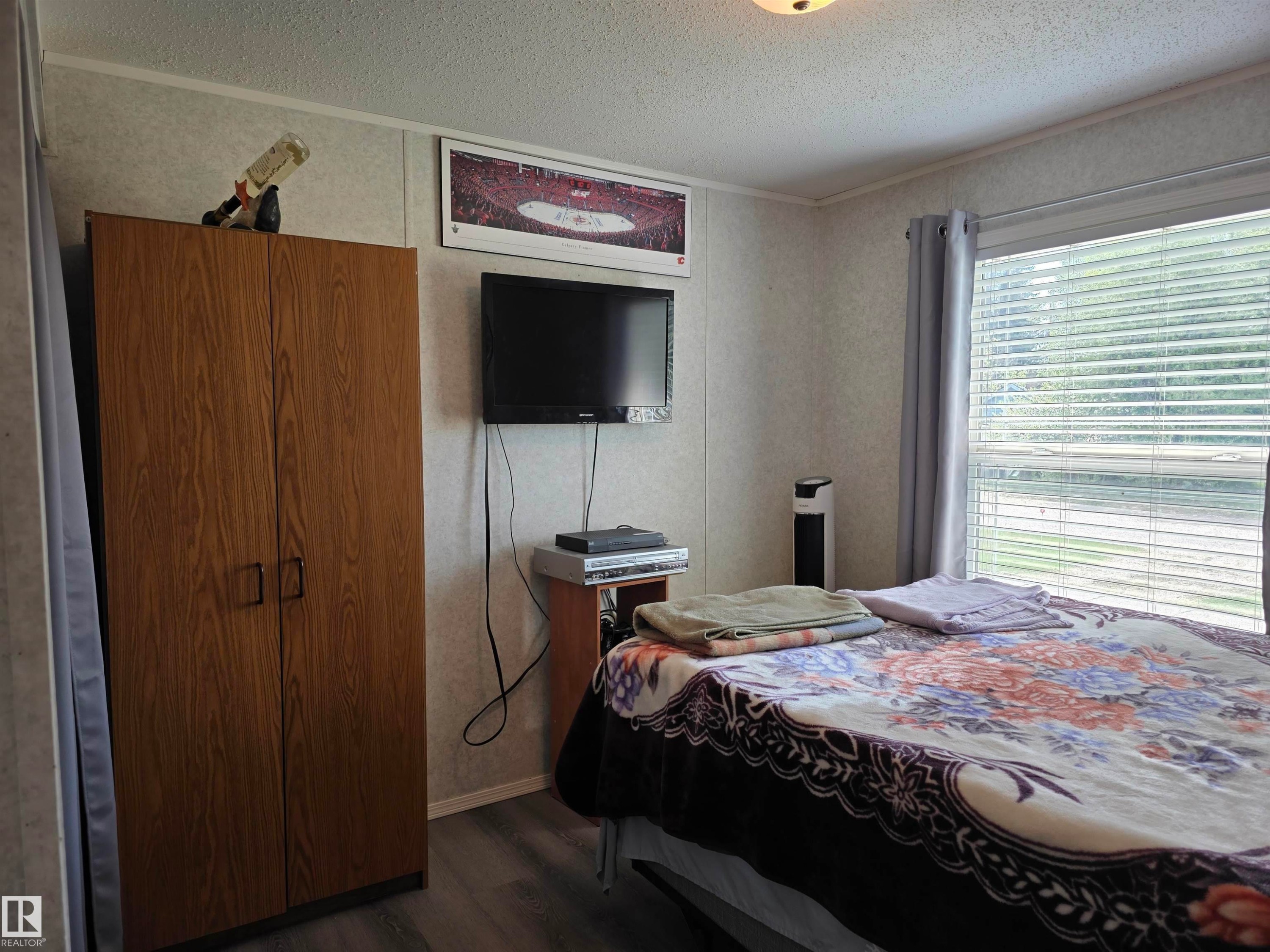 Bedroom featuring a large window with blinds, wood-finish flooring, and a ceiling light fixture - 5012 53 Ave, Breton, AB