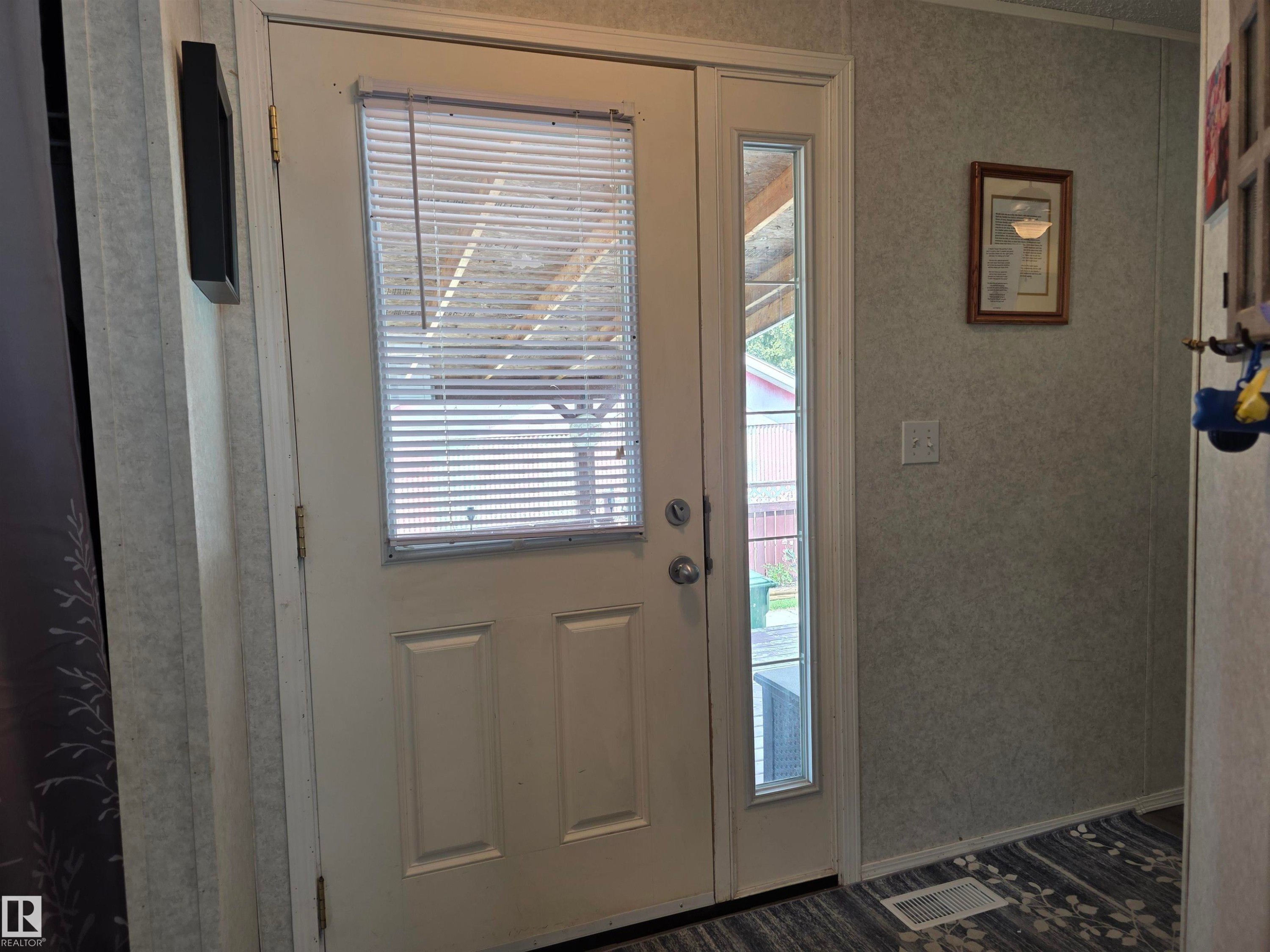 Entryway featuring a paneled door with integrated blinds, a full-length sidelight, textured wall panels, and patterned flooring - 5012 53 Ave, Breton, AB