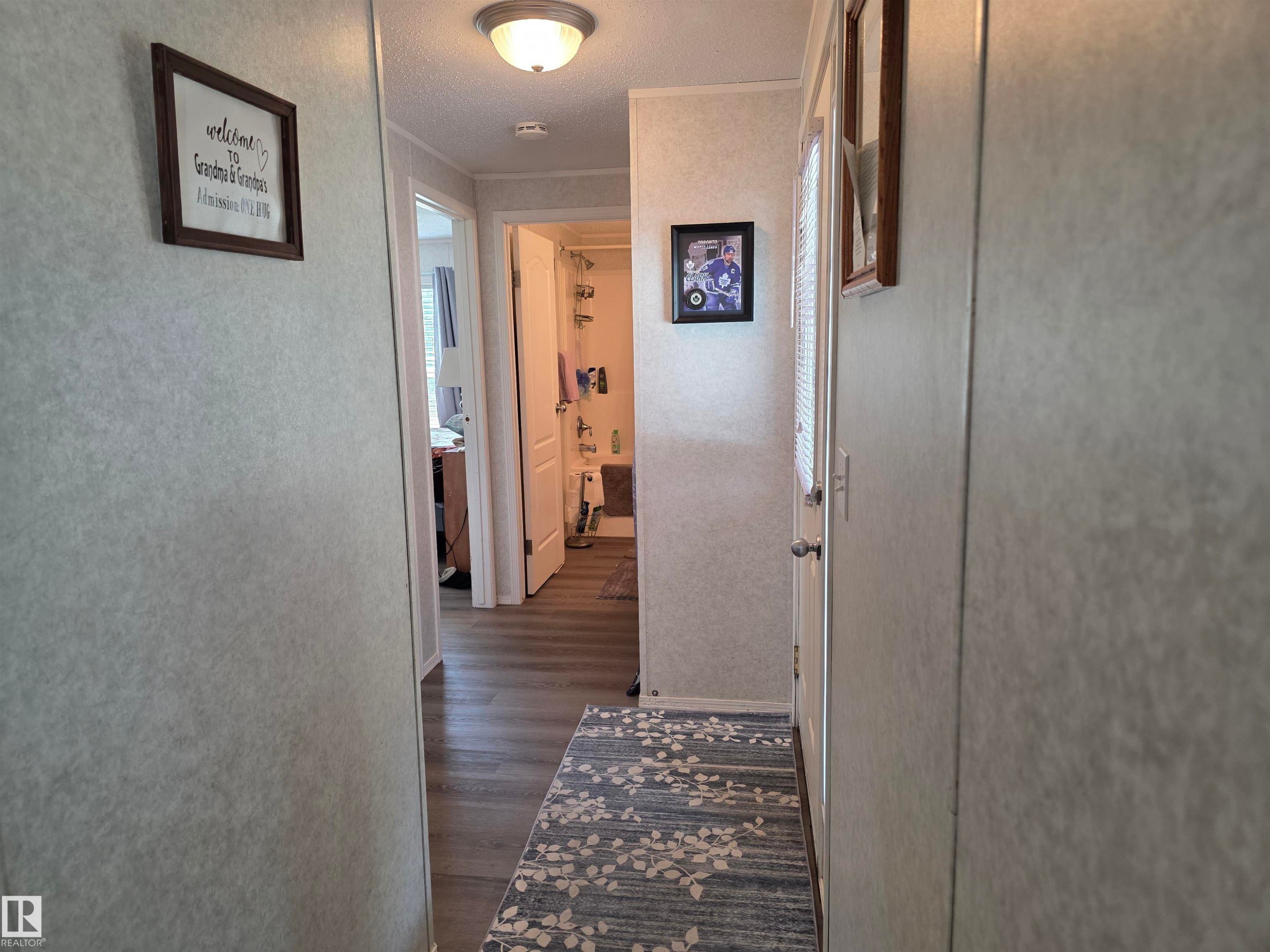 Hallway featuring wood-finish flooring, light-colored walls, and a ceiling-mounted flush light fixture - 5012 53 Ave, Breton, AB