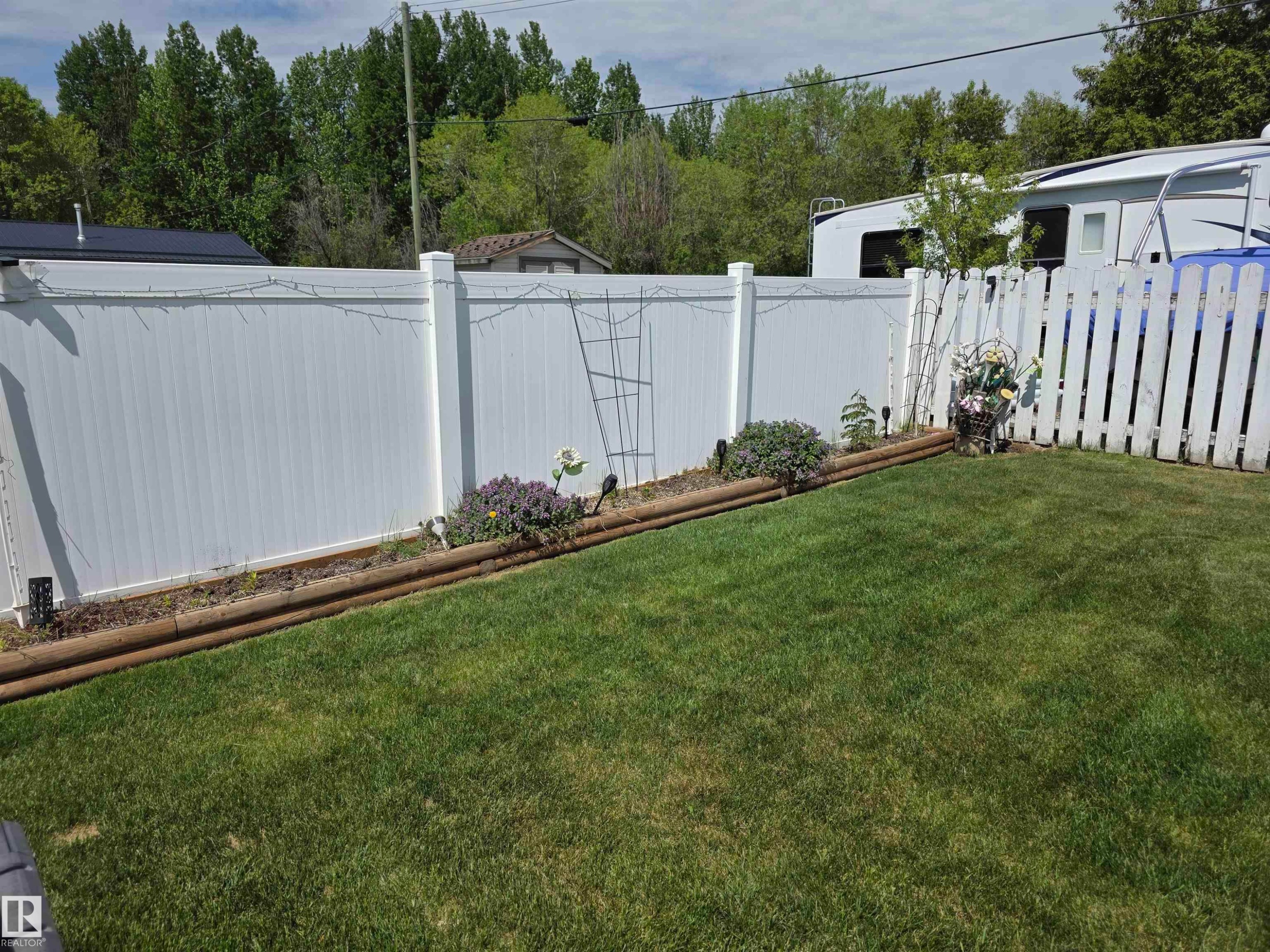 Manicured lawn with a white vinyl privacy fence and a white picket fence - 5012 53 Ave, Breton, AB