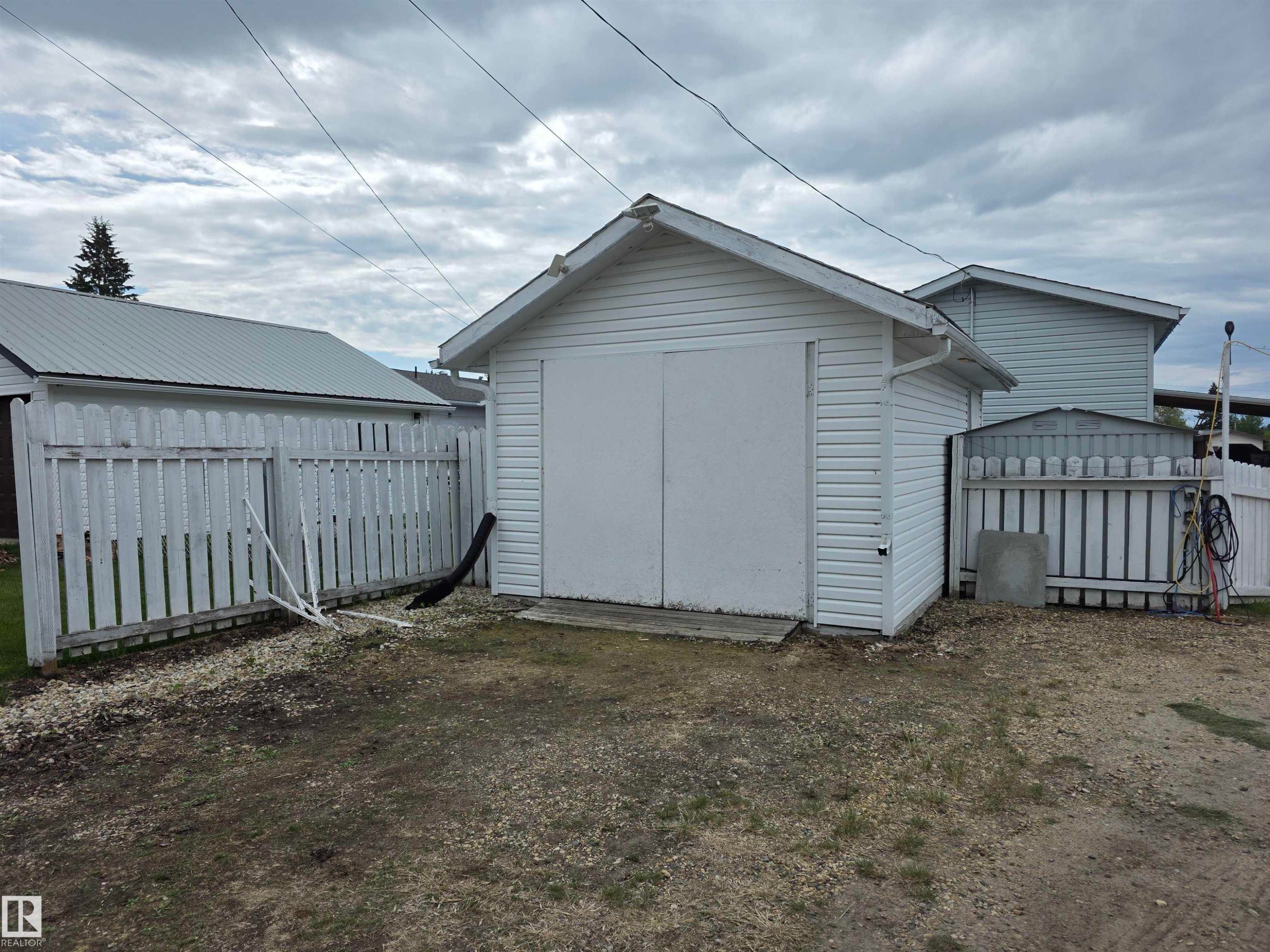 Detached garage with white siding and pitched roof, featuring double panel doors and an exterior side door - 5012 53 Ave, Breton, AB
