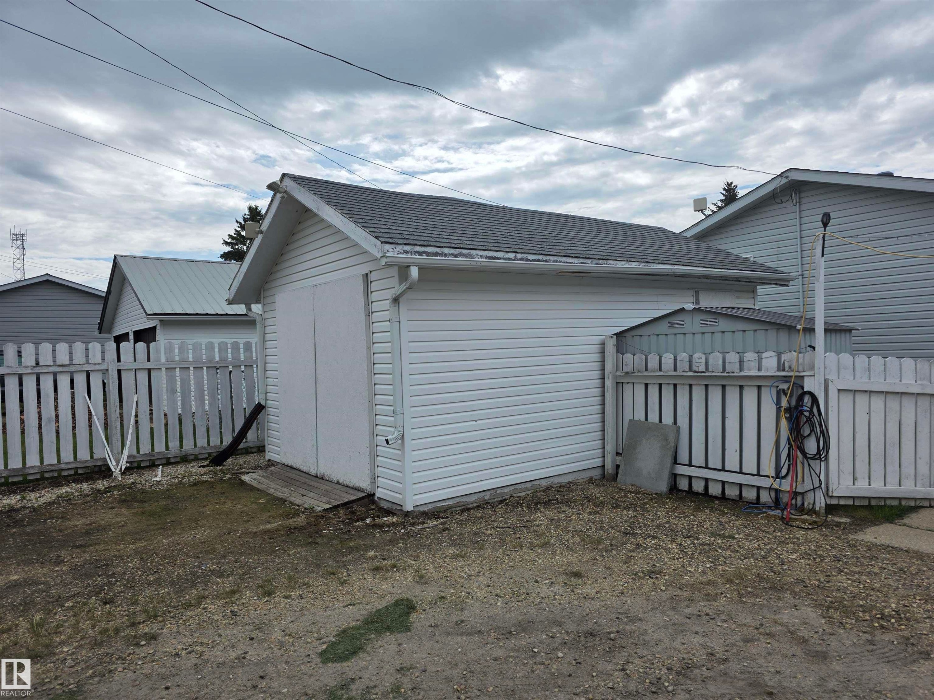 Detached garage with white vinyl siding, a gray shingle roof, and dual wooden swing-out doors - 5012 53 Ave, Breton, AB