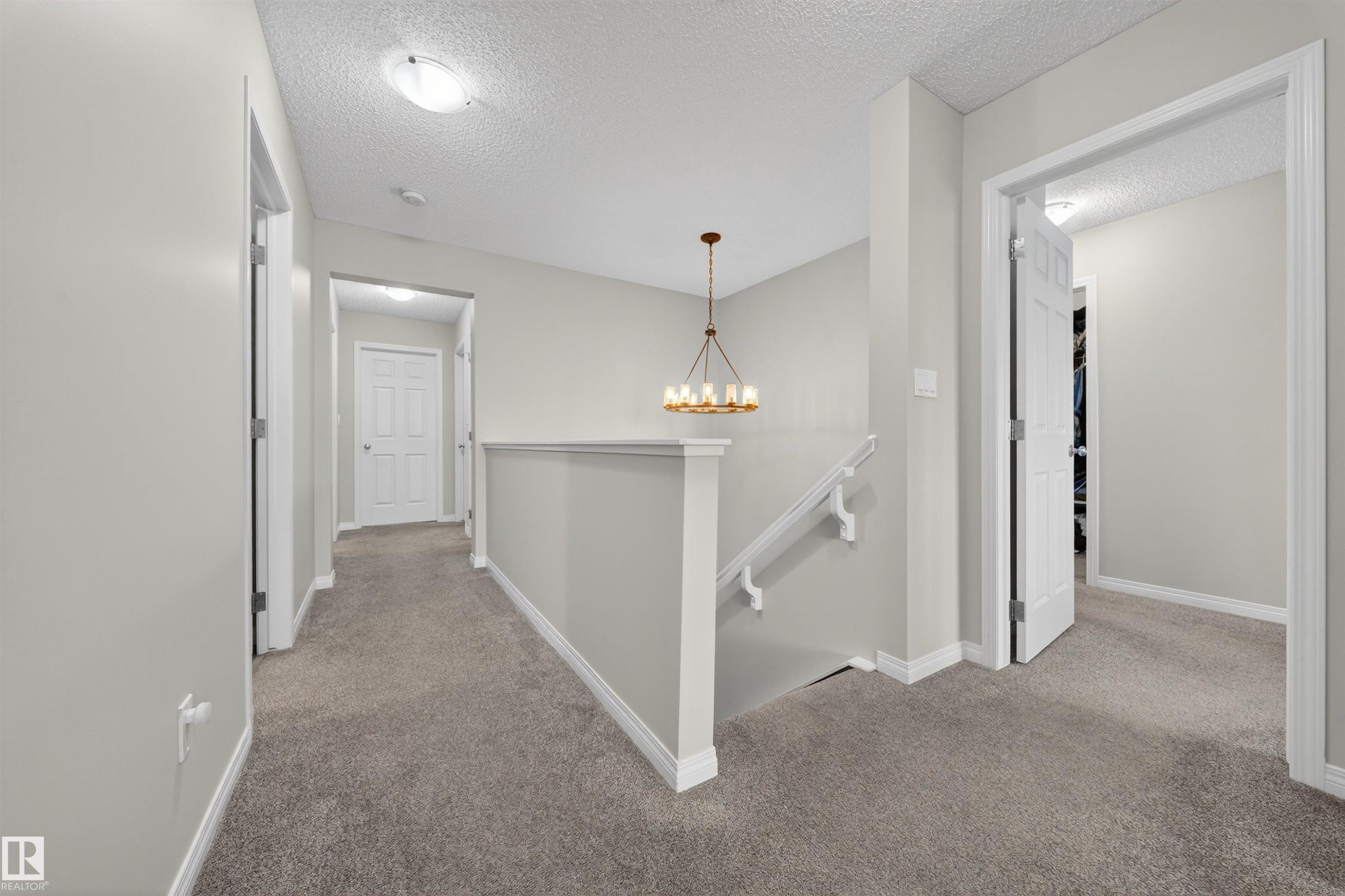 Upper-level landing featuring a bronze-finish chandelier, neutral carpet flooring, and white trim - 6085 King Landing, Edmonton, AB - Indoor Photo Showing Other Room
