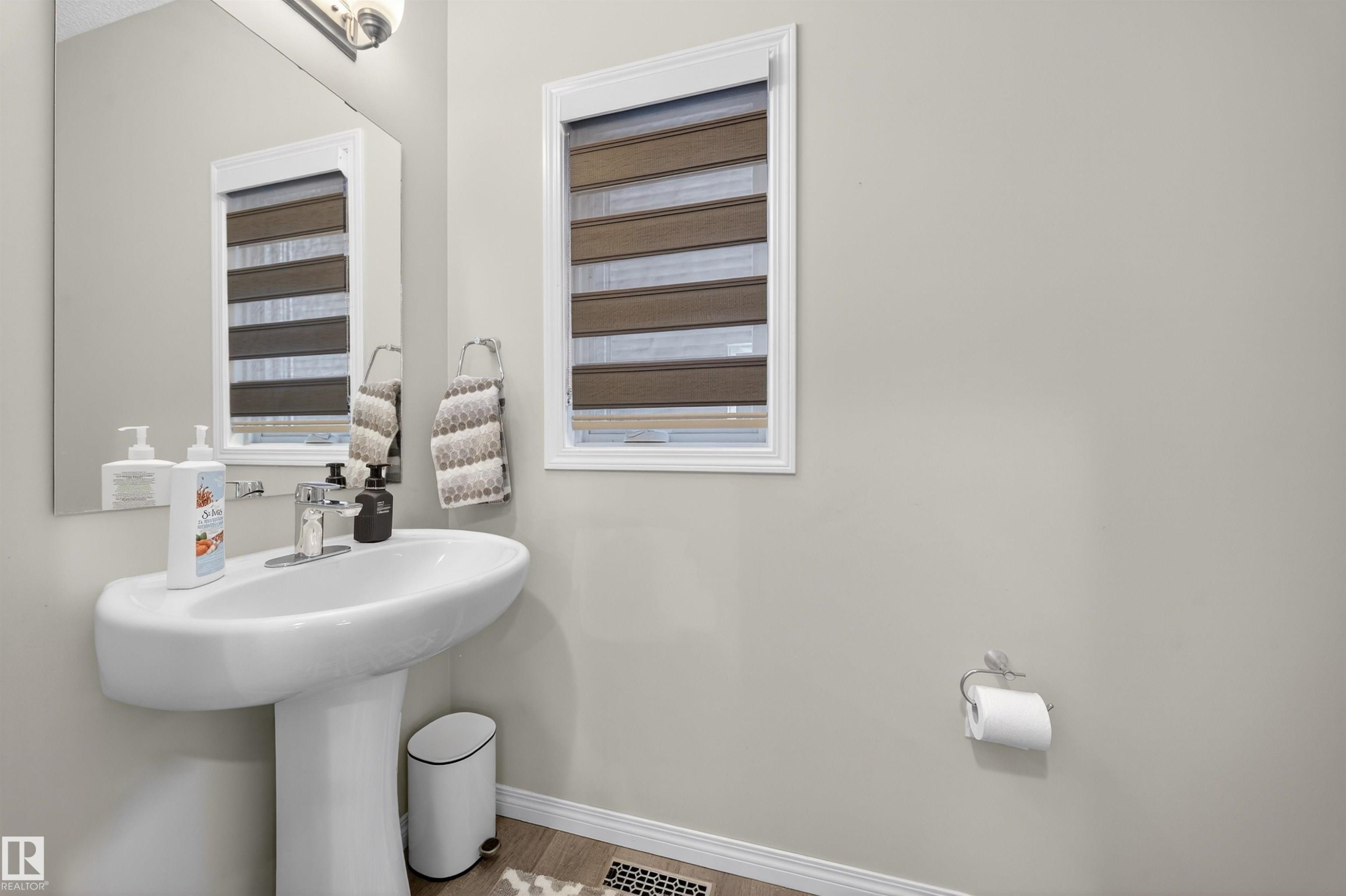 Pedestal sink with chrome faucet, a rectangular mirror, and a window with horizontal blinds - 6085 King Landing, Edmonton, AB - Indoor Photo Showing Bathroom