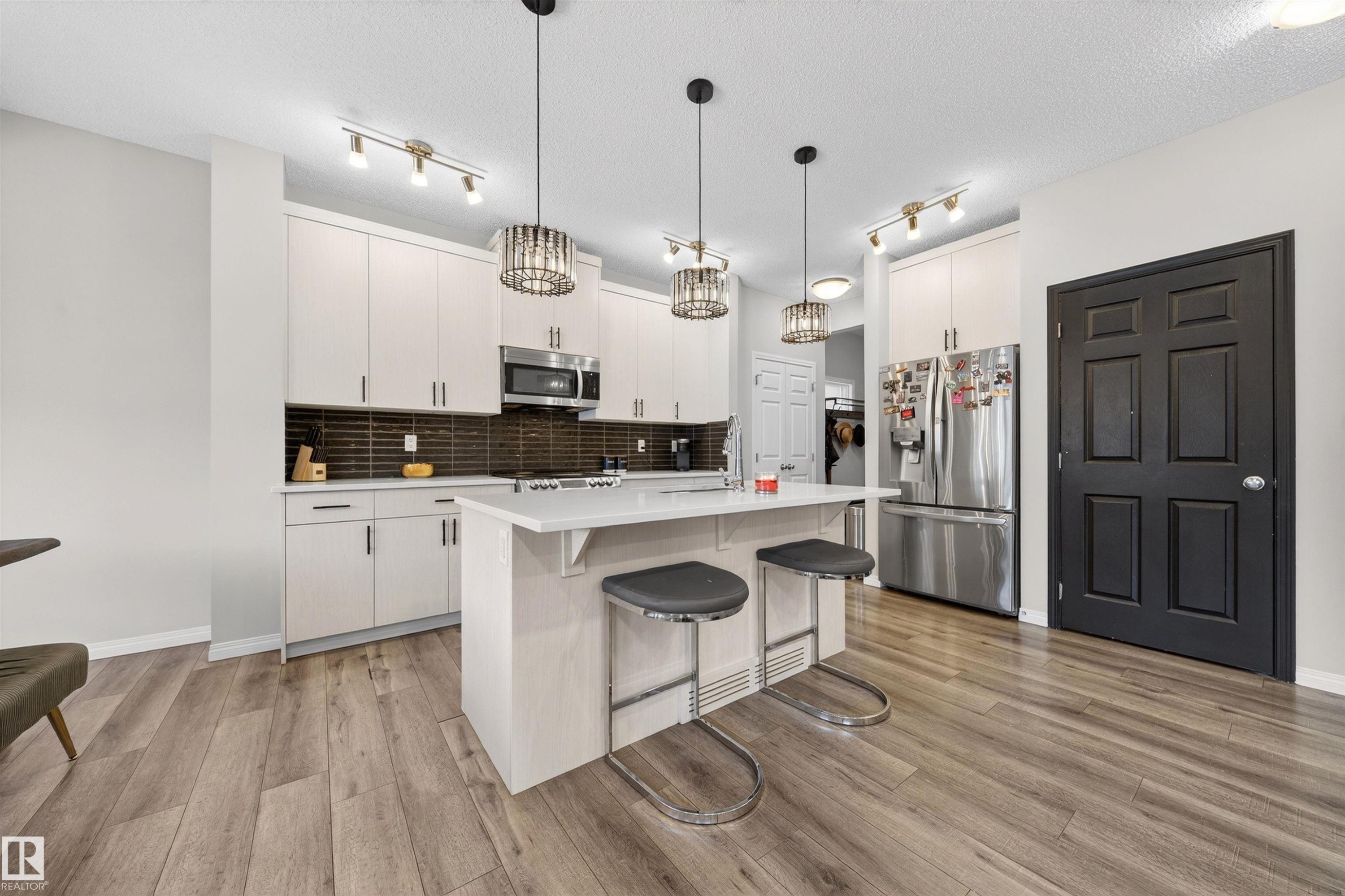 Kitchen featuring light-toned cabinetry, stainless steel appliances, a center island with seating, dark subway tile backsplash, and wood-finish flooring - 6085 King Landing, Edmonton, AB - Indoor Photo Showing Kitchen With Upgraded Kitchen